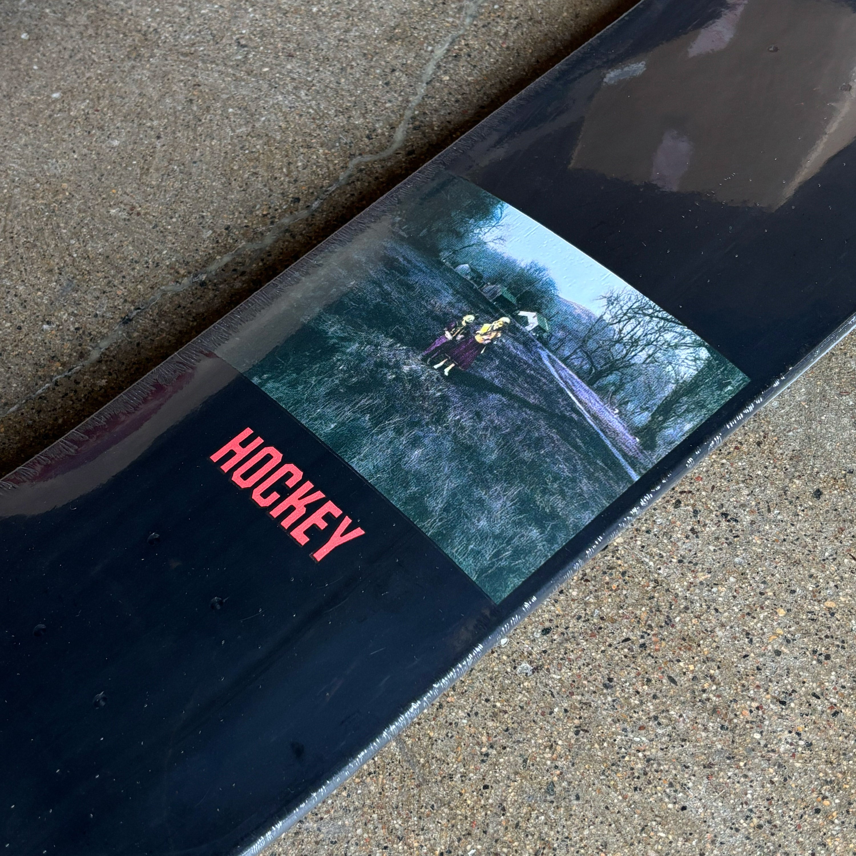 Close-up of a hockey stick with a scene of two people on skis and the word 'HOCKEY' on a concrete surface.