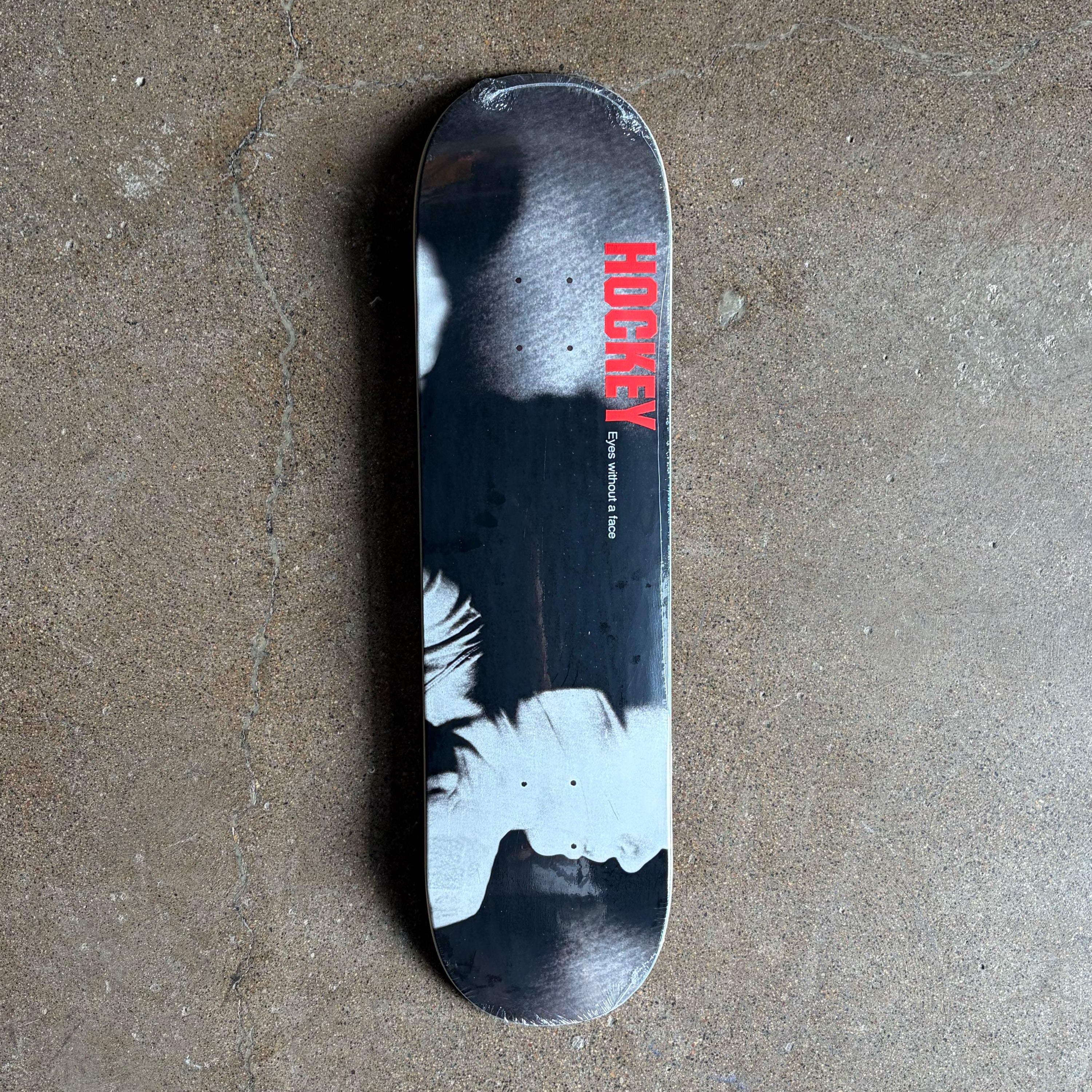 A hockey skate deck with a black and white graphic design and red 'HOCKEY' text, photographed from above on a textured concrete floor.