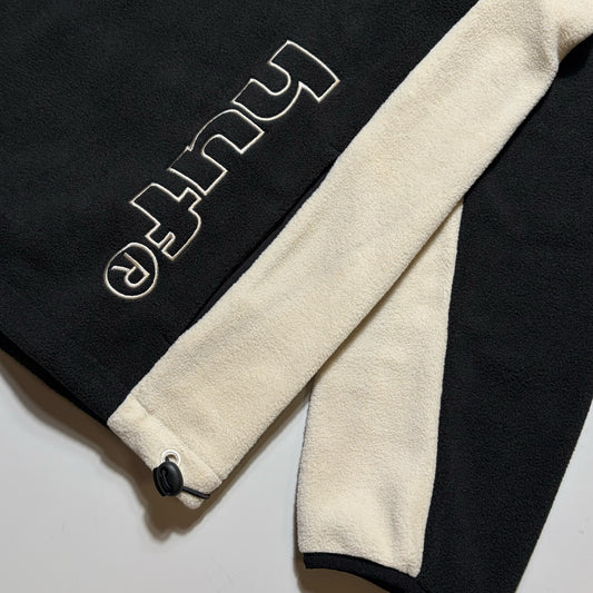 Close-up of a black fleece garment with a thick cream-colored lining and white embroidered text reading 'HUF' on the sleeve.