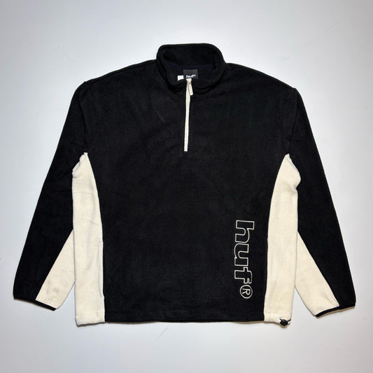 A black and off-white colorblock quarter-zip polar fleece pullover Huf, featuring off-white contrast panels on the sleeves and a vertical white 'HUF' logo on the lower right side.