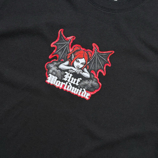 Close-up of a black t-shirt featuring a graphic print of a red-haired angel with bat wings and the text 'HUF Worldwide' in white gothic lettering.