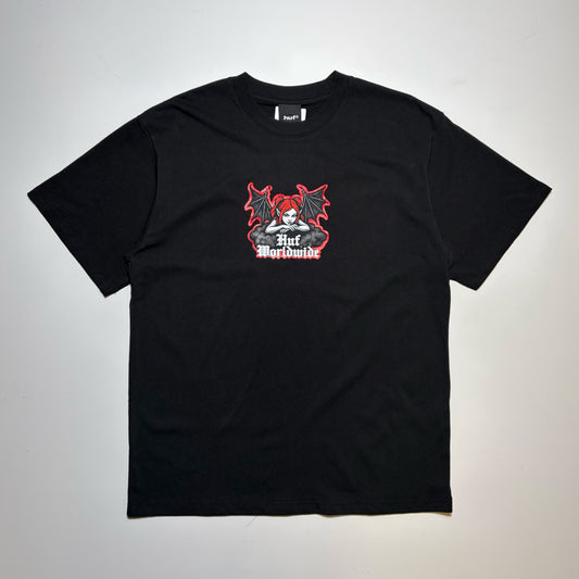 A black short-sleeve t-shirt with a graphic on the chest featuring a skull and red devil wings, with the text 'HUF Worldwide' printed below it, laid flat on a light gray background.