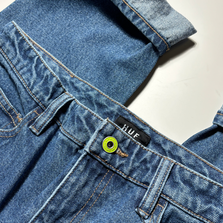 Close detail of denim. Green button closure with gold contrast stitch and cuffed.