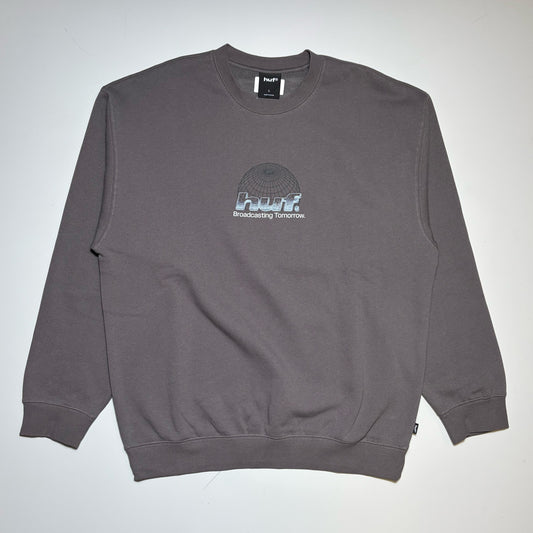 A dark gray crewneck sweatshirt with a small 'HUF' graphic on the center chest, laid flat against a light gray background.