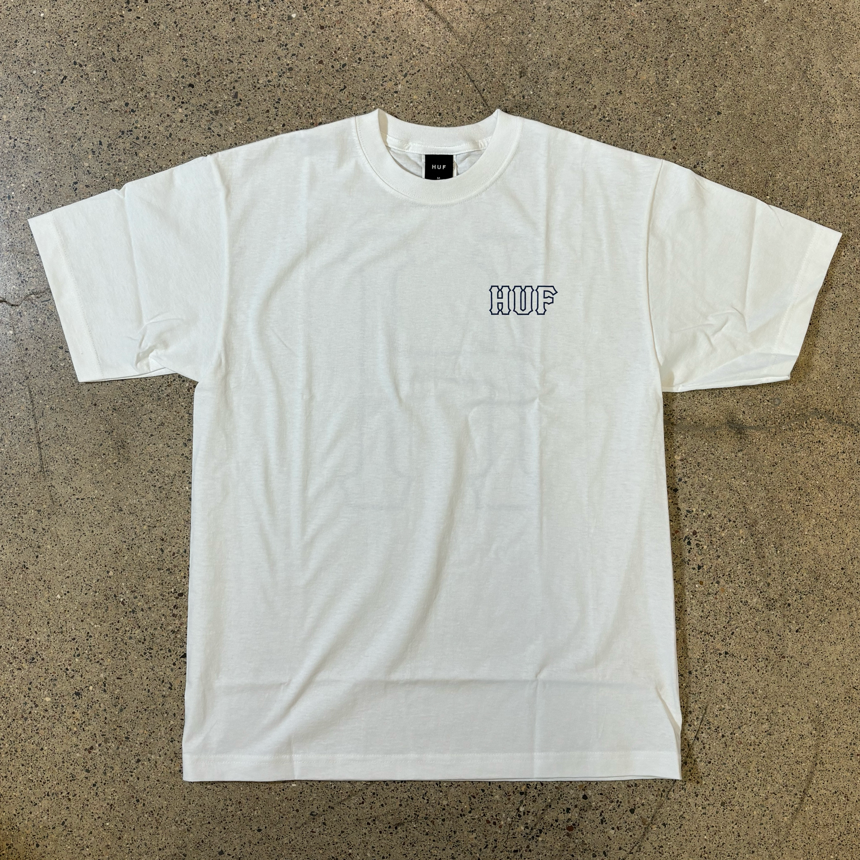 WHITE T-SHIRT, BOLD OUTLINE FONT THAT READS HUF ON LEFT SIDE CHEST