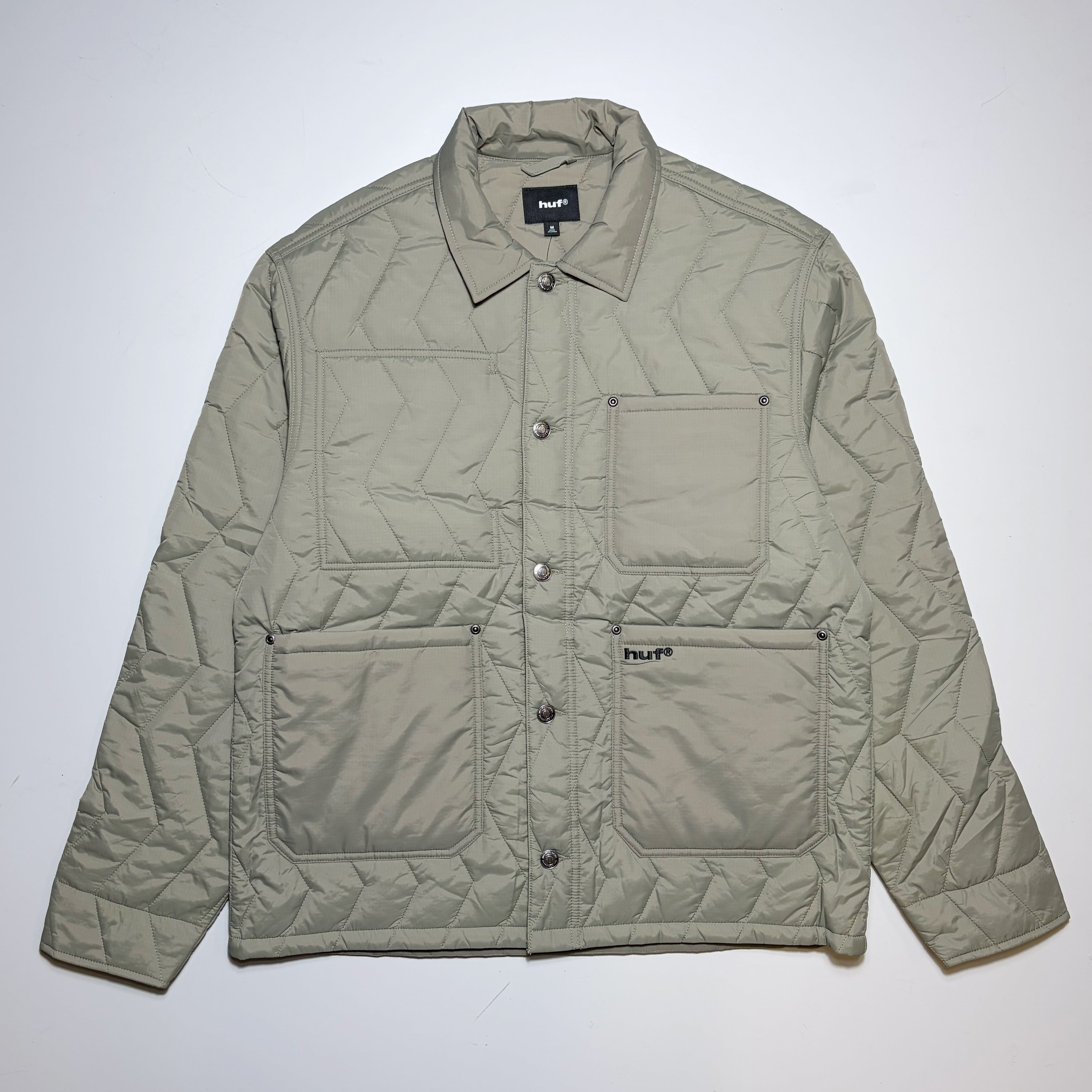 Full image, HUF zig-zag quilted chore jacket with custom button and embroidered logo on pocket. 