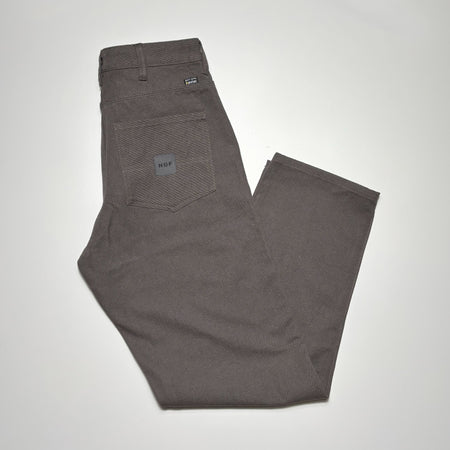 Image of folded pant in cement grey with HUF woven label on back pocket.