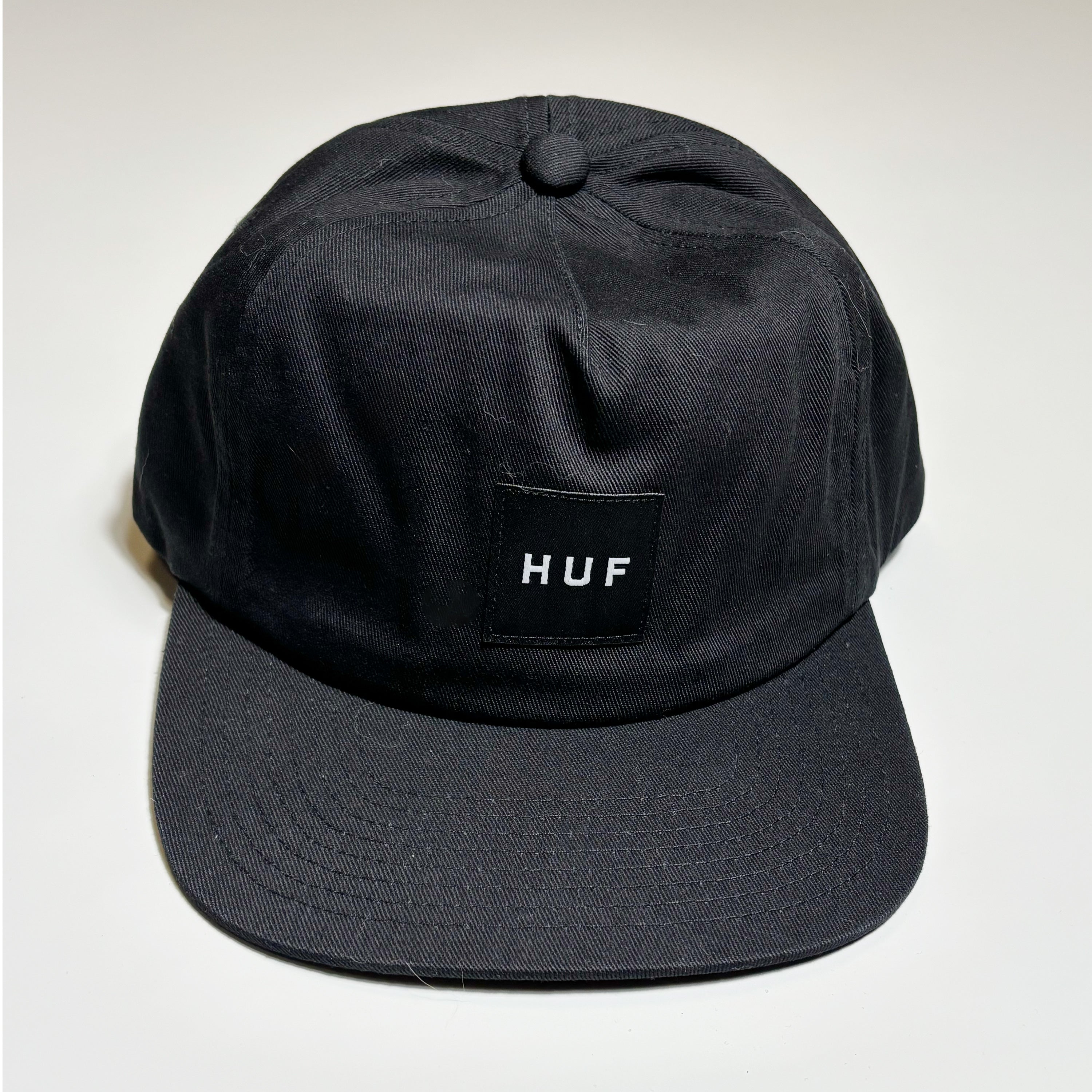 Front image of black twill hat with woven label on crown.