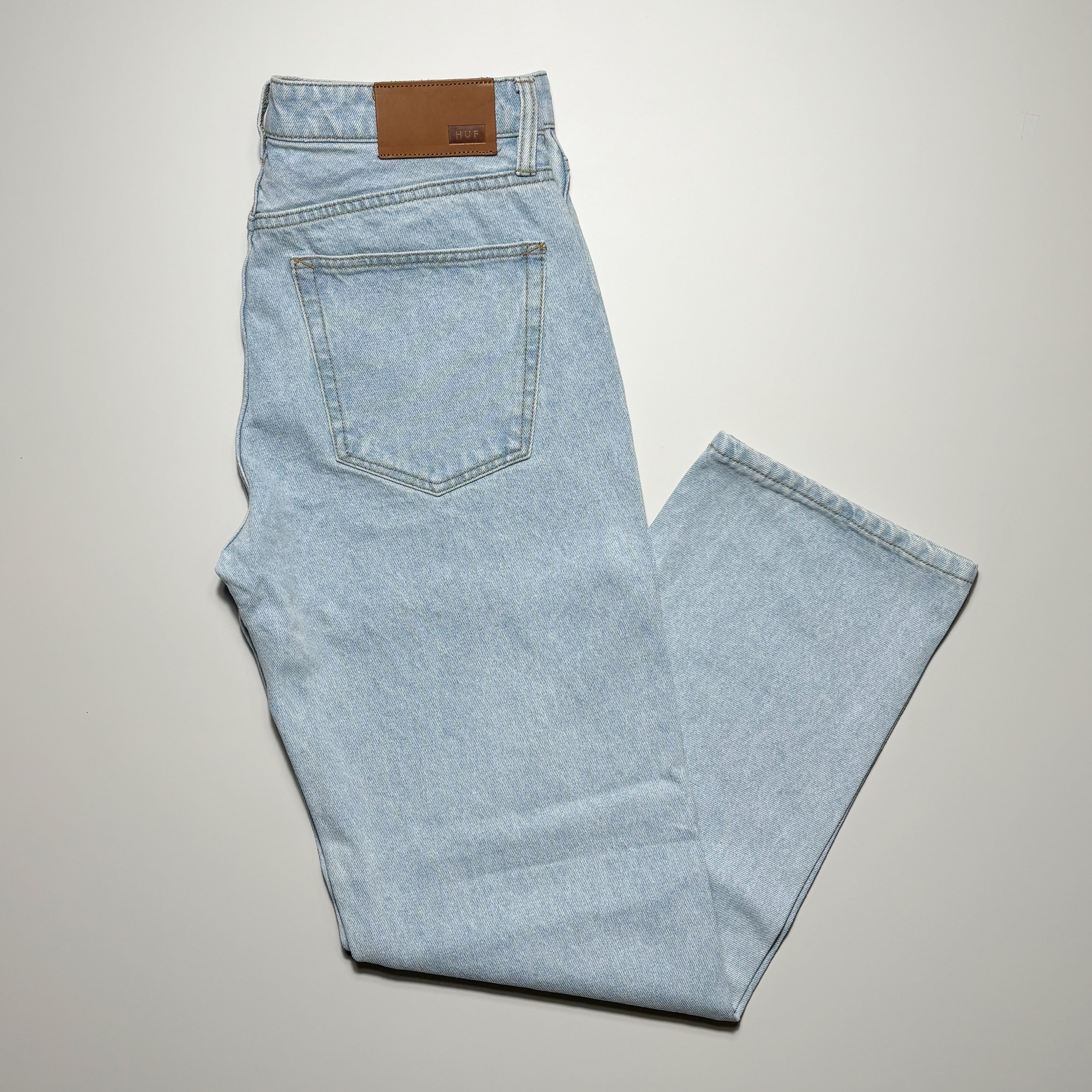 Folded image of light blue jean denim with leather embossed patch on waist.
