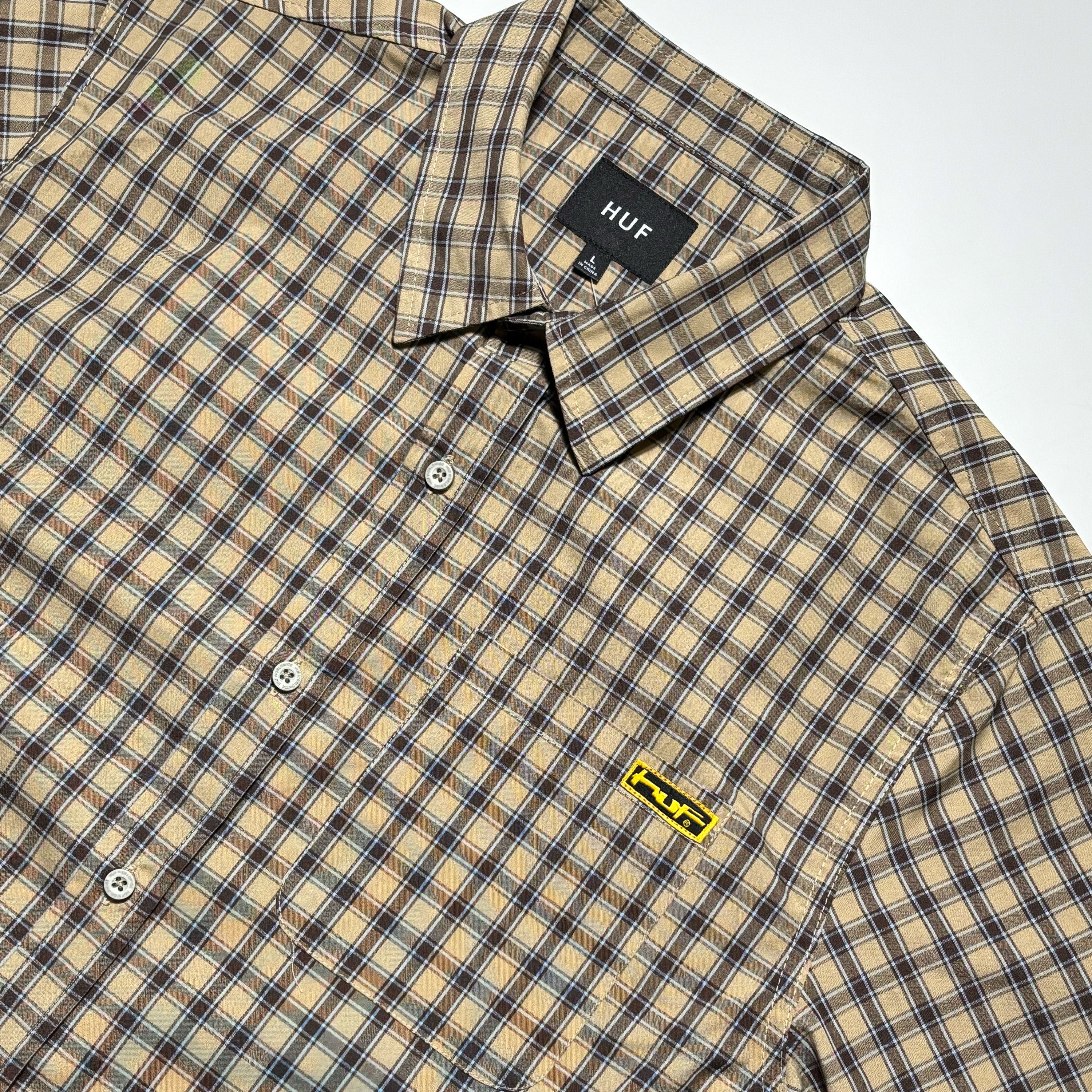 Close detail of plaid shirt with HUF label on chest.