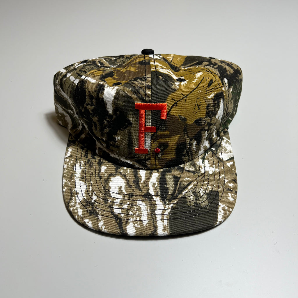 Front facing unstructured 6 panel camo print hat with embroidered F. logo in orange and red. 