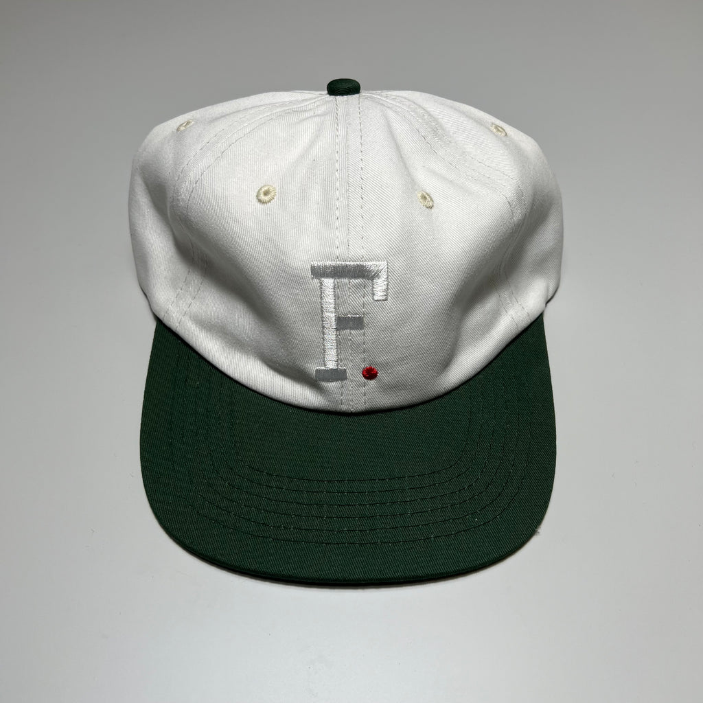 Front facing unstructured 6 panel hat in white and green bill with white embroidered F and red embroidered dot.