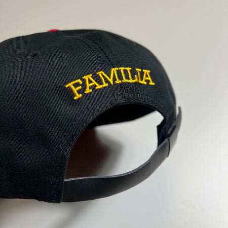 Unstructured 6 panel hat in black and red with yellow embroidered familia logo on the back above the leather strap.