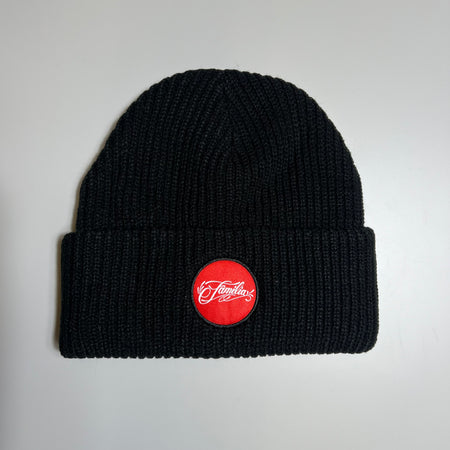 Full image of black beanie with folded  cuff. Red woven familia patch centered.