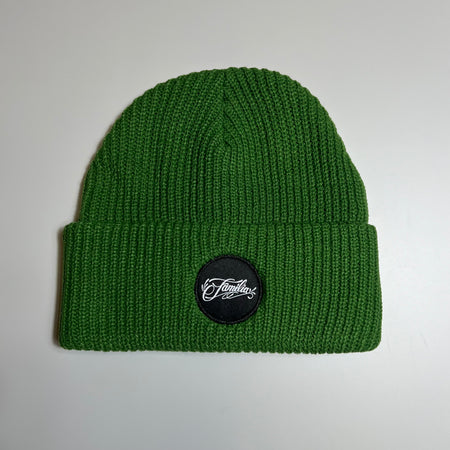 Full image of green beanie with folded  cuff. Black woven familia patch centered.