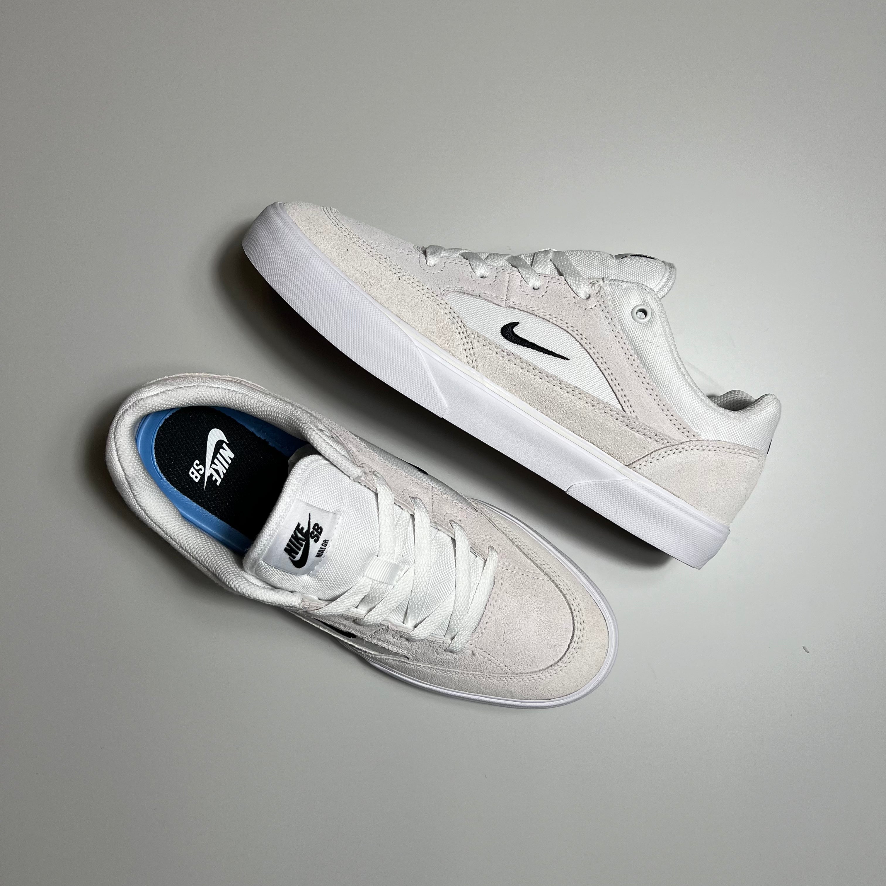 Side and top view of the Nike SB Malor shoes in summit white with black embroidered check logo and white gum sole.