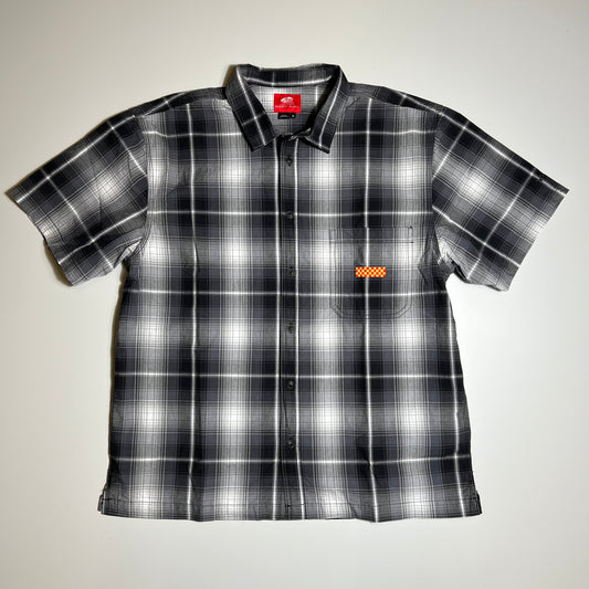 Front facing button up shirt in black and white plaid with a yellow and red tag on left side chest pocket.
