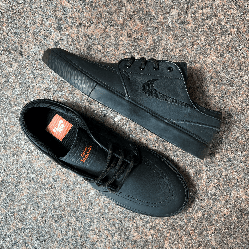 NIKE SB JANOSKI SHOES IN BLACK LEATHER, BLACK EMBROIDERED SWOOSH LOGO AND BLACK SOLE DISPLAYED ON GRANITE