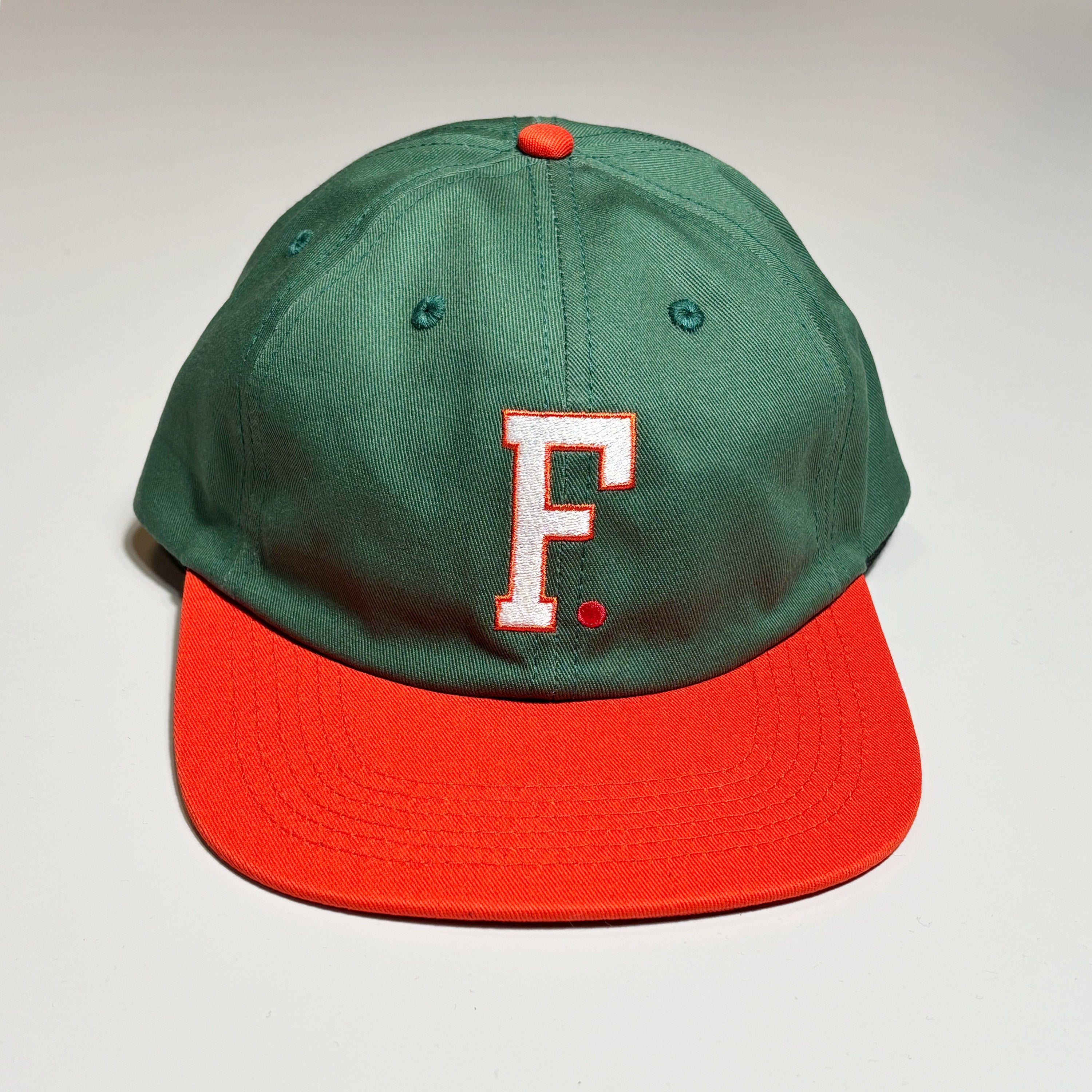 Front image of green hat with orange bill.
White embroidered F with orange outline and red dot. 