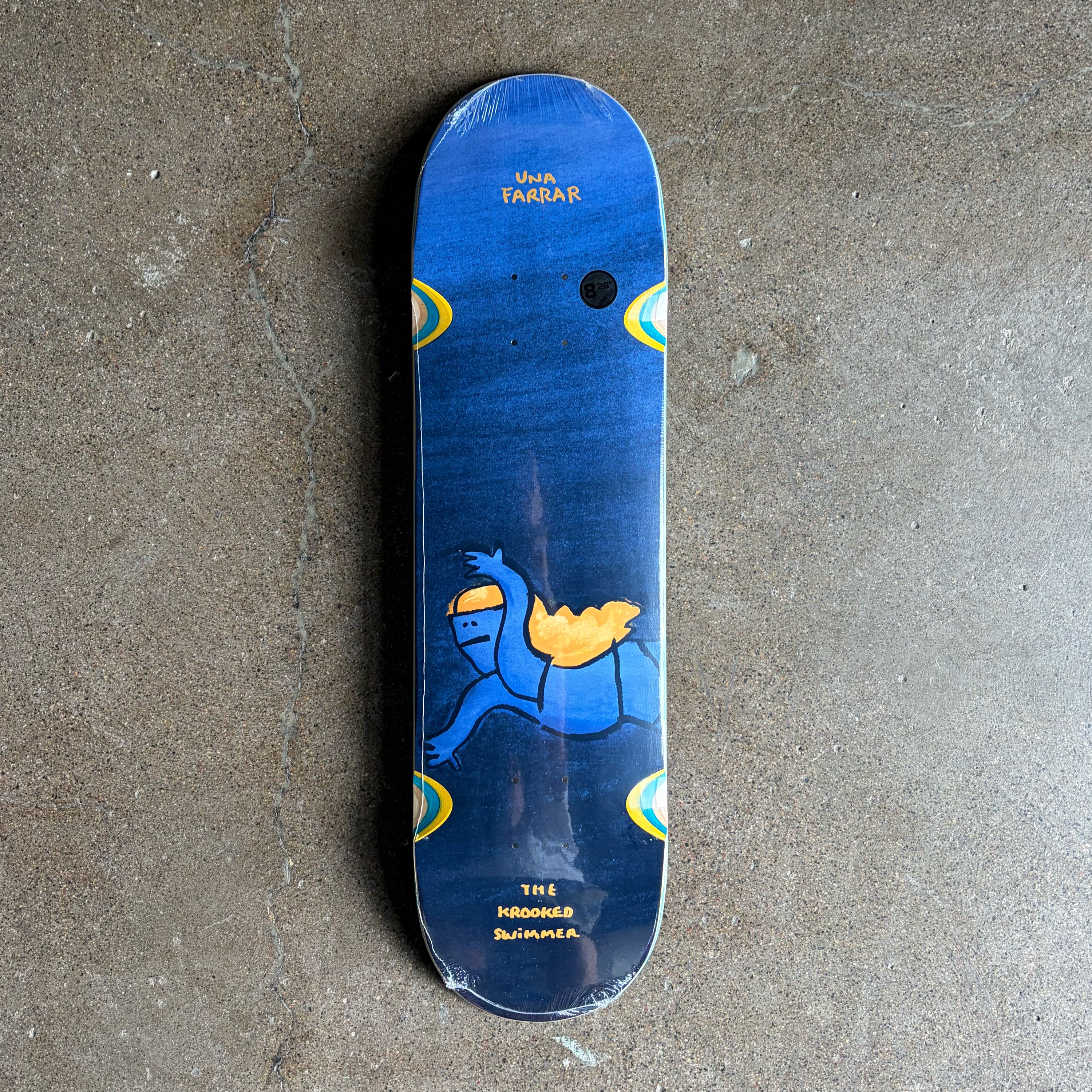 A Krooked skateboard deck with a blue background and a cartoon knight graphic, photographed flat on a concrete floor.