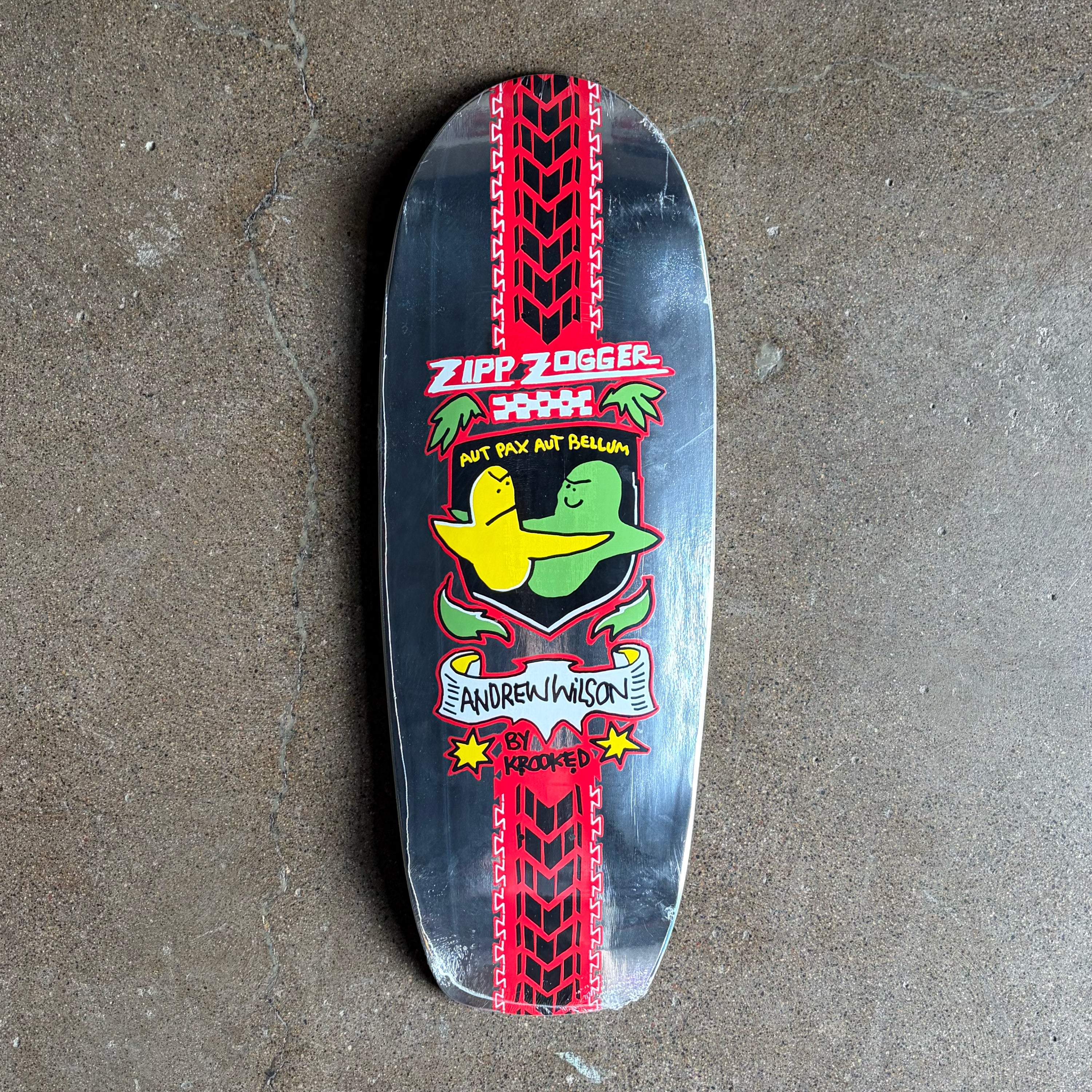 A custom skateboard deck featuring a black background with red tire tracks, a green and yellow duck mascot, and text reading 'Zip Zogger' and 'Andrei Iwanon by Krewed' on a concrete floor.