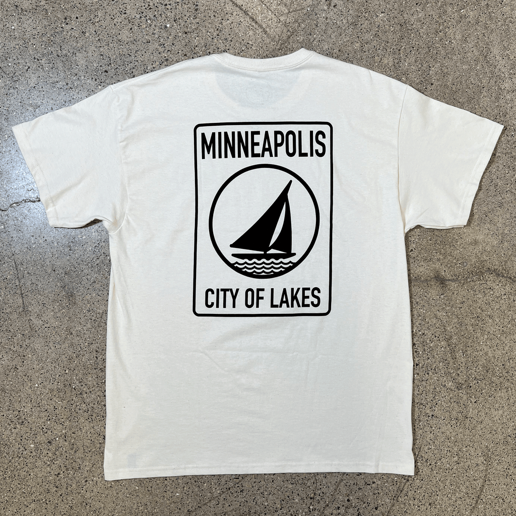 BLACK SIDE OF CREAM T-SHIRT WITH WHITE GRAPHIC OF A SAILBOAT THAT SAYS MINNEAPOLIS CITY OF LAKES