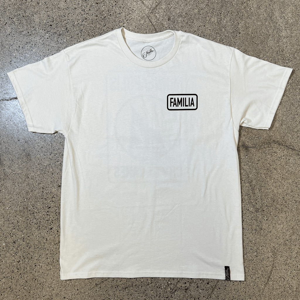 FRONT SIDE OF A CREAM T-SHIRT WITH A WHITE GRAPHIC THAT READS FAMILIA ON THE LEFT CHEST SIDE