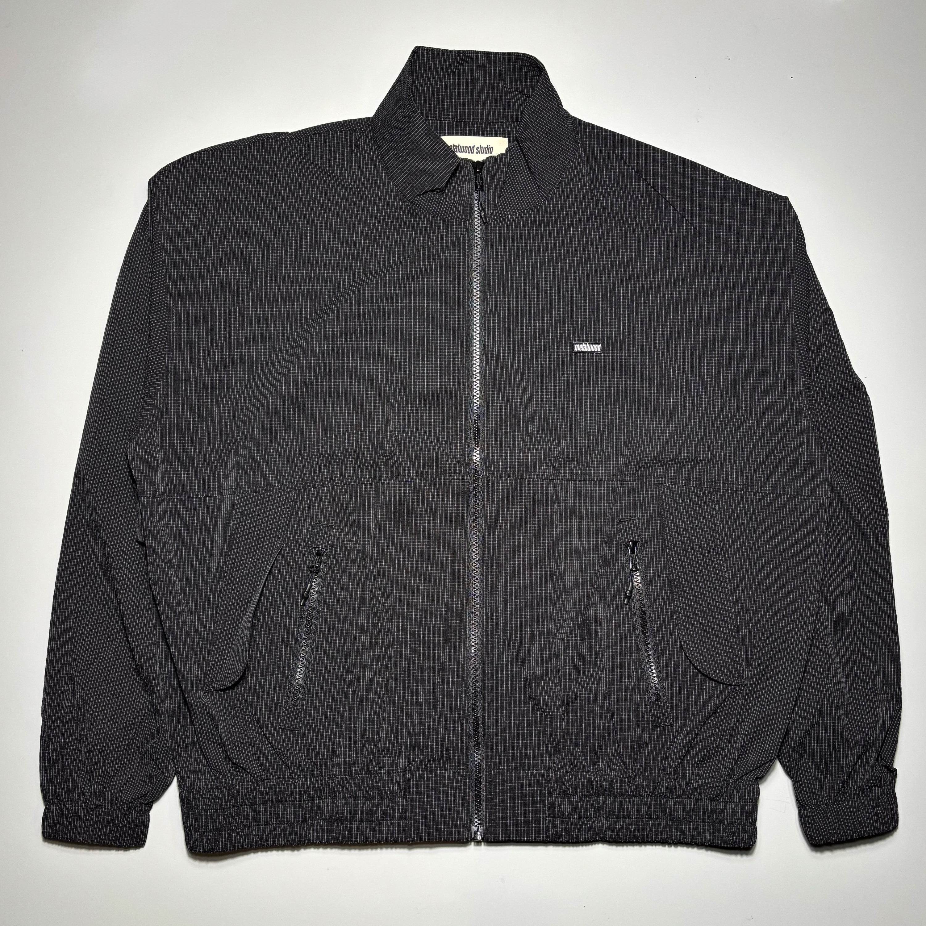 Front image of black track jacket with metalwood label on chest.