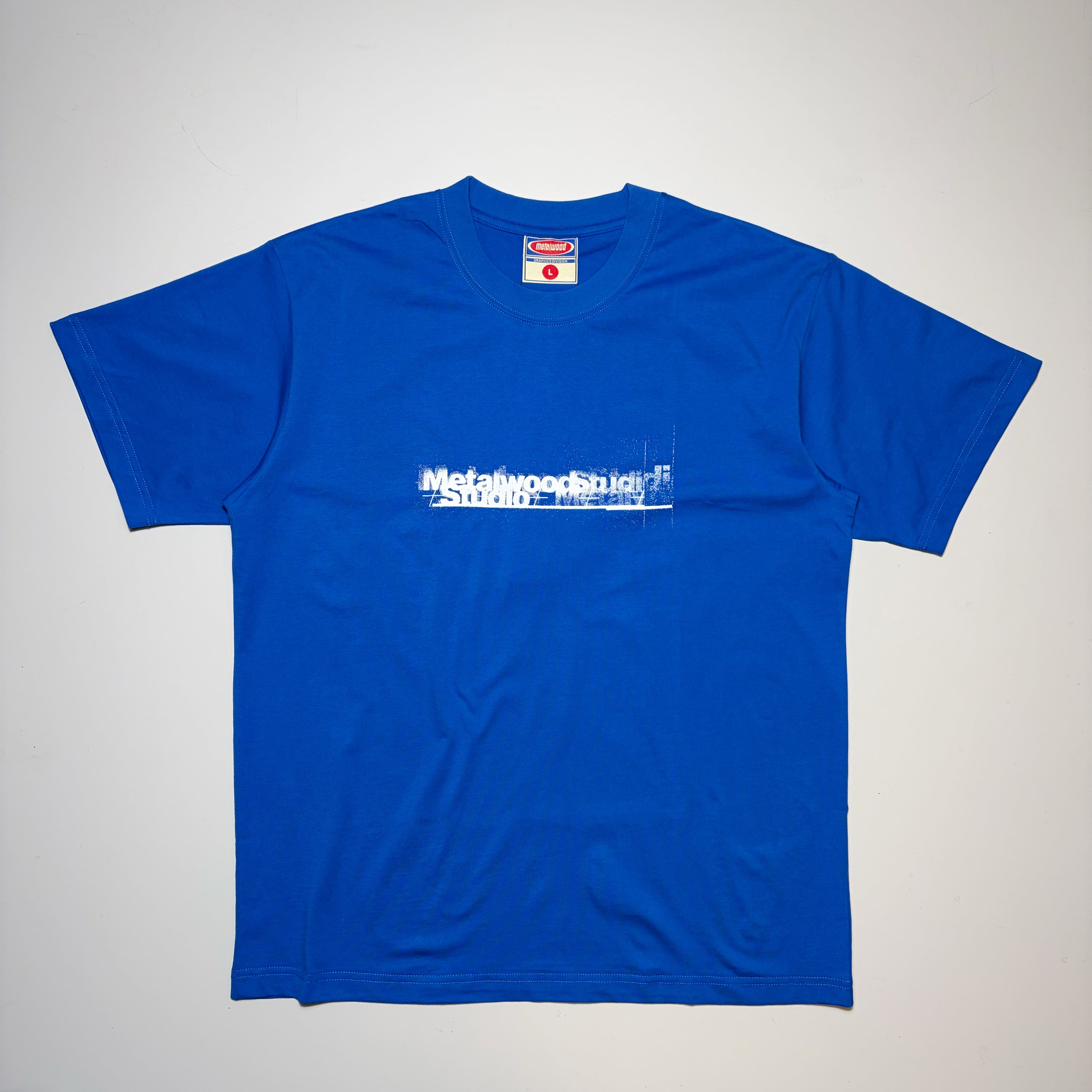 Full image of Metalwood Studio Premium Golf Apparel. Blue cotton tee with white logo printed on chest.