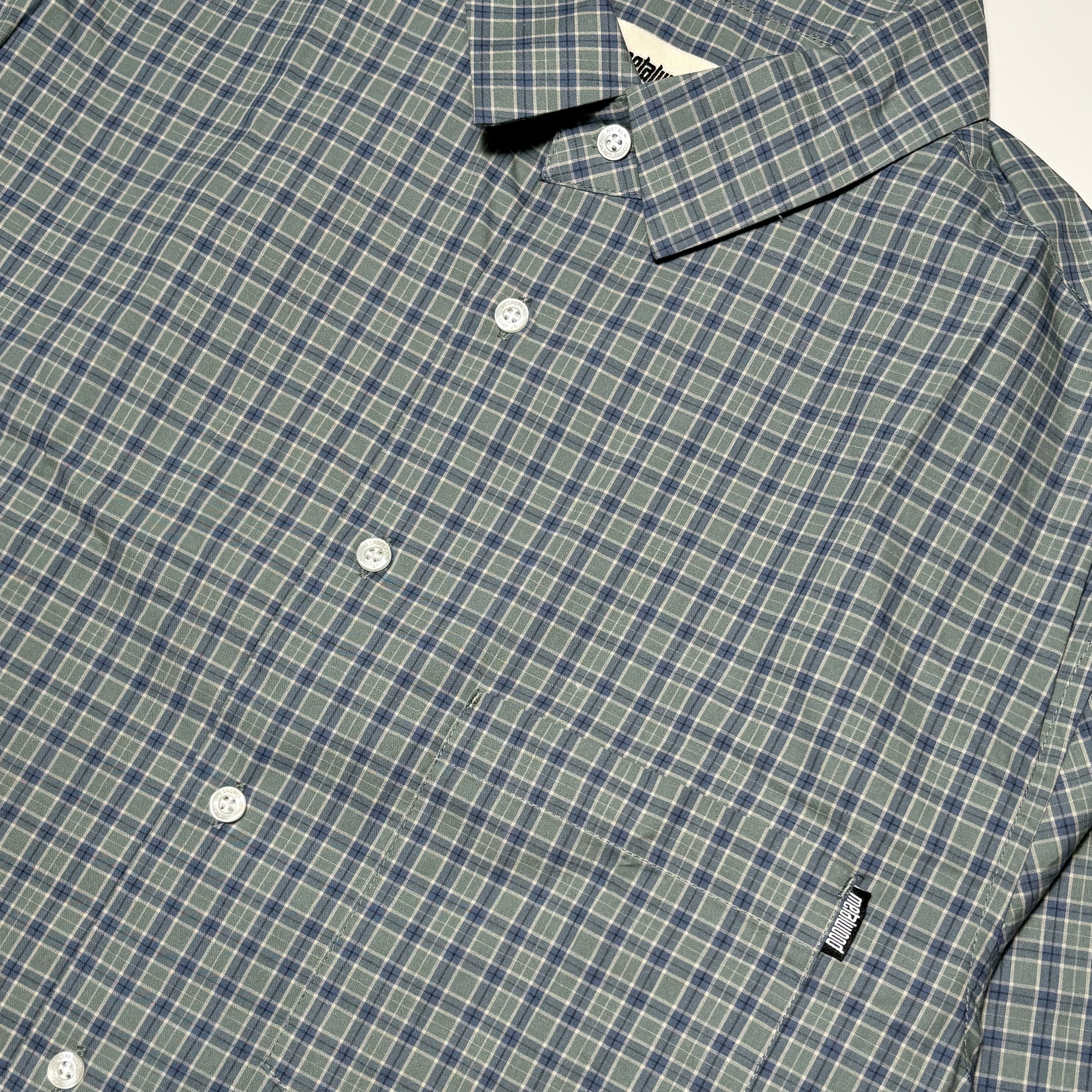 Close detail of pine green checker print shirt with metalwood label on pocket.
