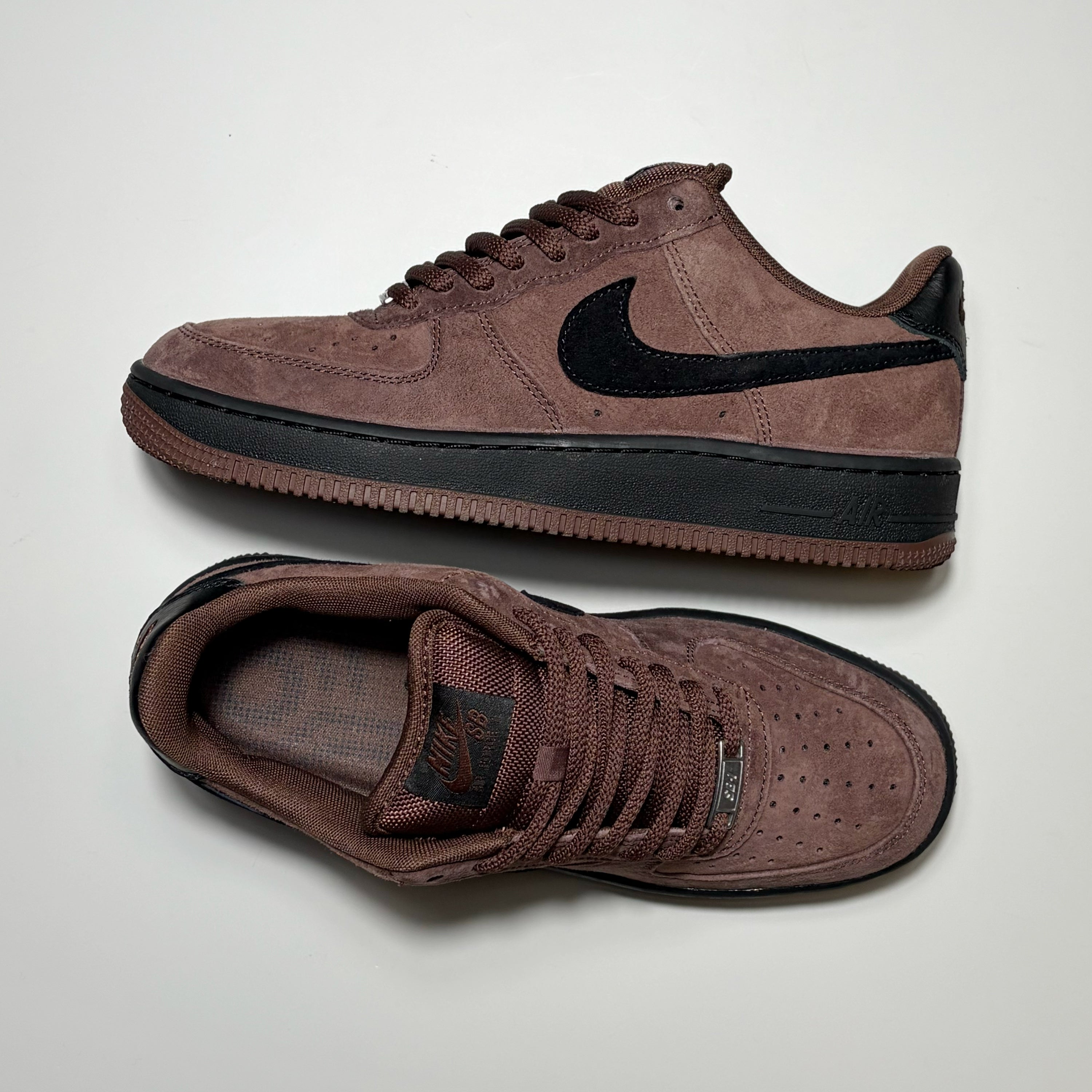 A pair of Nike SB Air Force 1 Low sneakers in a dark brown suede and mesh upper with a black Swoosh and black midsole, displayed on a light gray background.