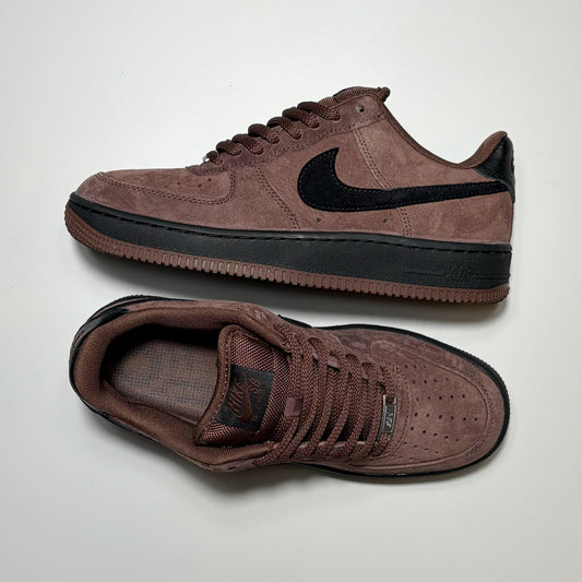 A pair of Nike SB Air Force 1 Low sneakers in a dark brown suede and mesh upper with a black Swoosh and black midsole, displayed on a light gray background.
