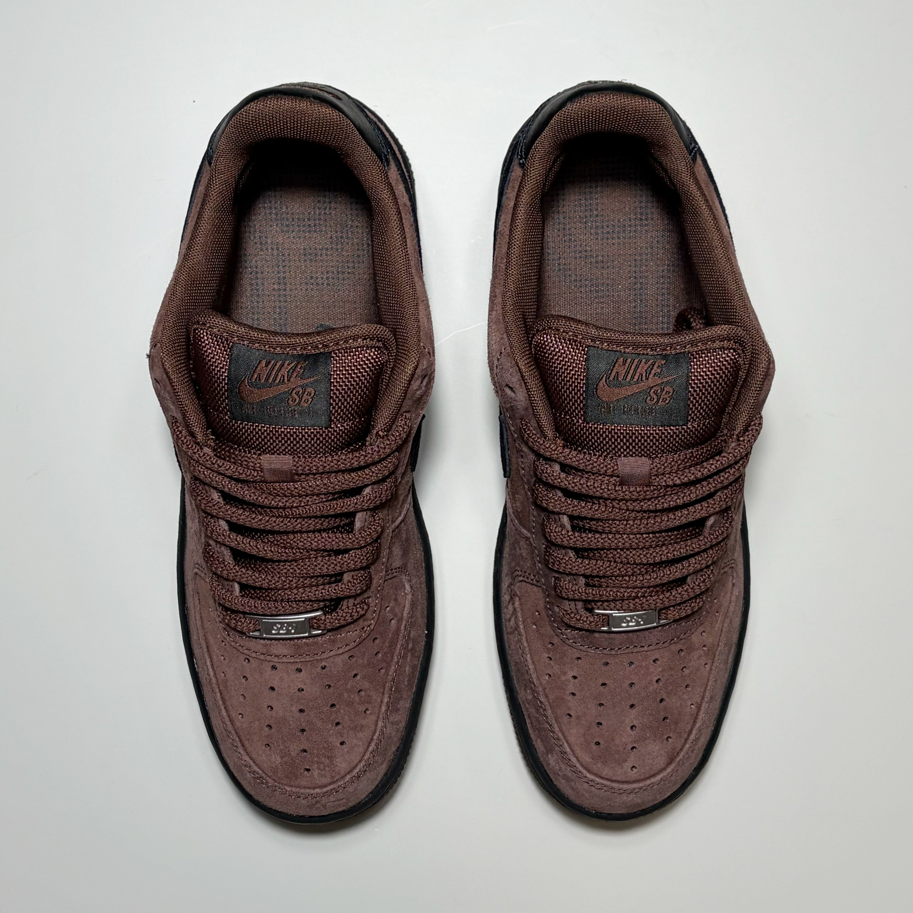 A pair of Nike SB Air Force 1 Low sneakers in a dark brown suede and mesh upper, shown from a top-down view on a light gray background.