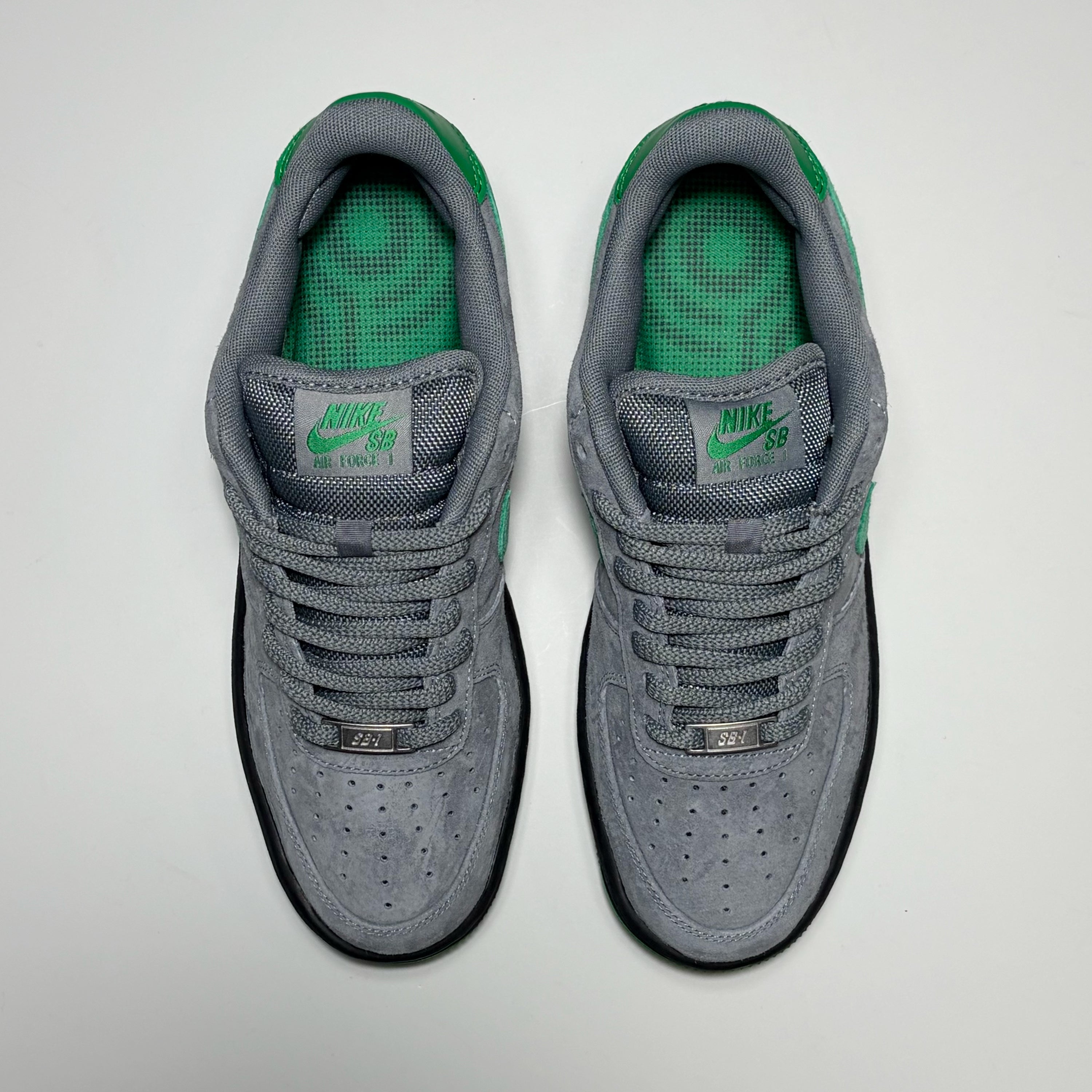 A pair of Nike SB Air Force 1 Low sneakers in gray suede and mesh with bright green accents on the tongue, heel, and collar lining, shown from a top-down view on a light gray background.