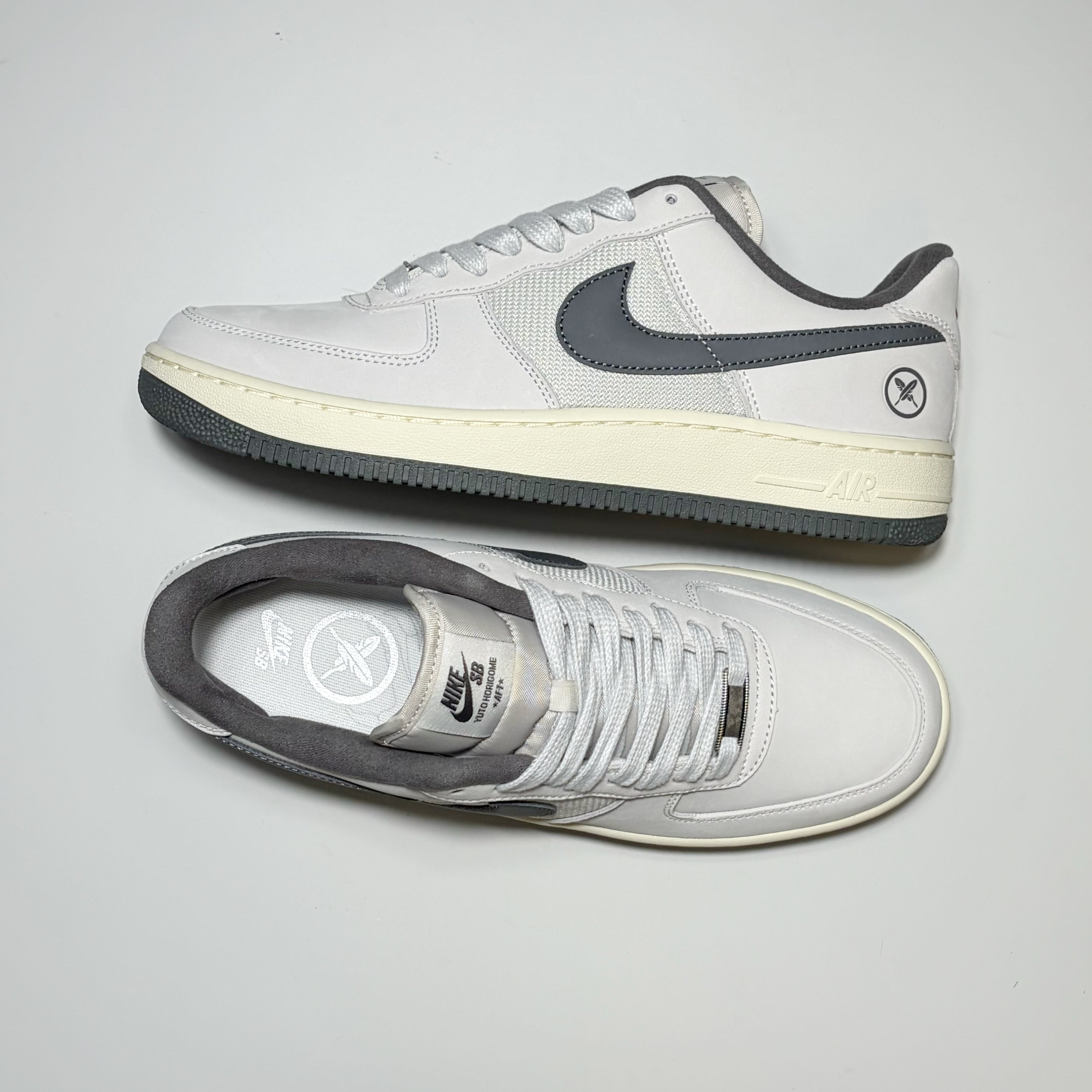 A pair of Nike SB Air Force 1 Low Yuto Horigome sneakers in white and dark gray, featuring a white leather upper, dark gray Swoosh and collar, and a cream-colored midsole.