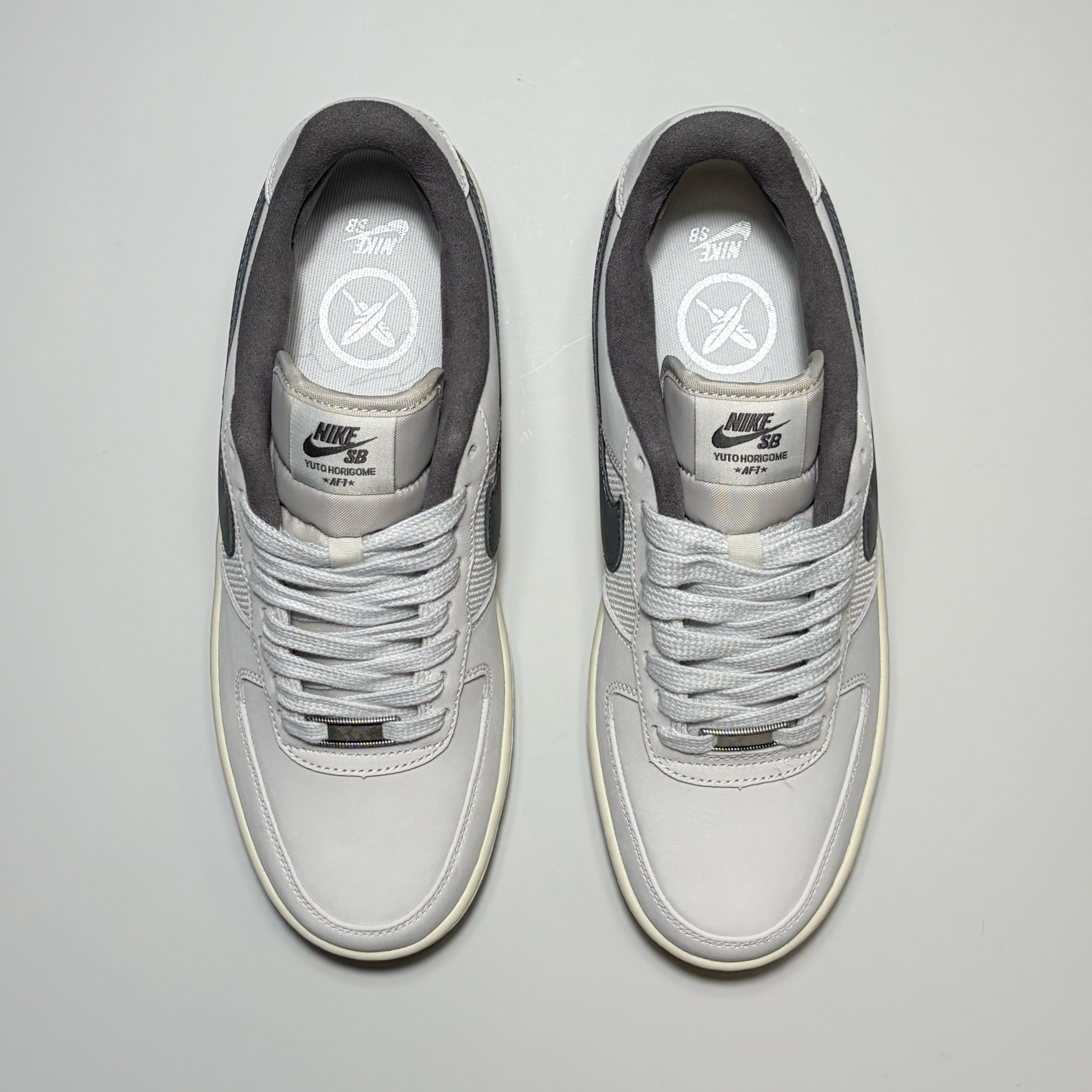 A pair of Nike SB Air Force 1 Low sneakers in light gray and white, shown from a top-down view on a light gray background.