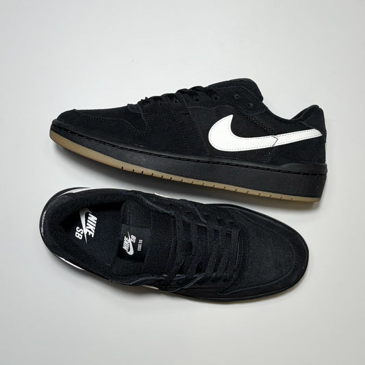A pair of Nike SB Code 58 Low sneakers in black suede, featuring a white Swoosh on the side and a gum-colored rubber sole, displayed on a light gray background.