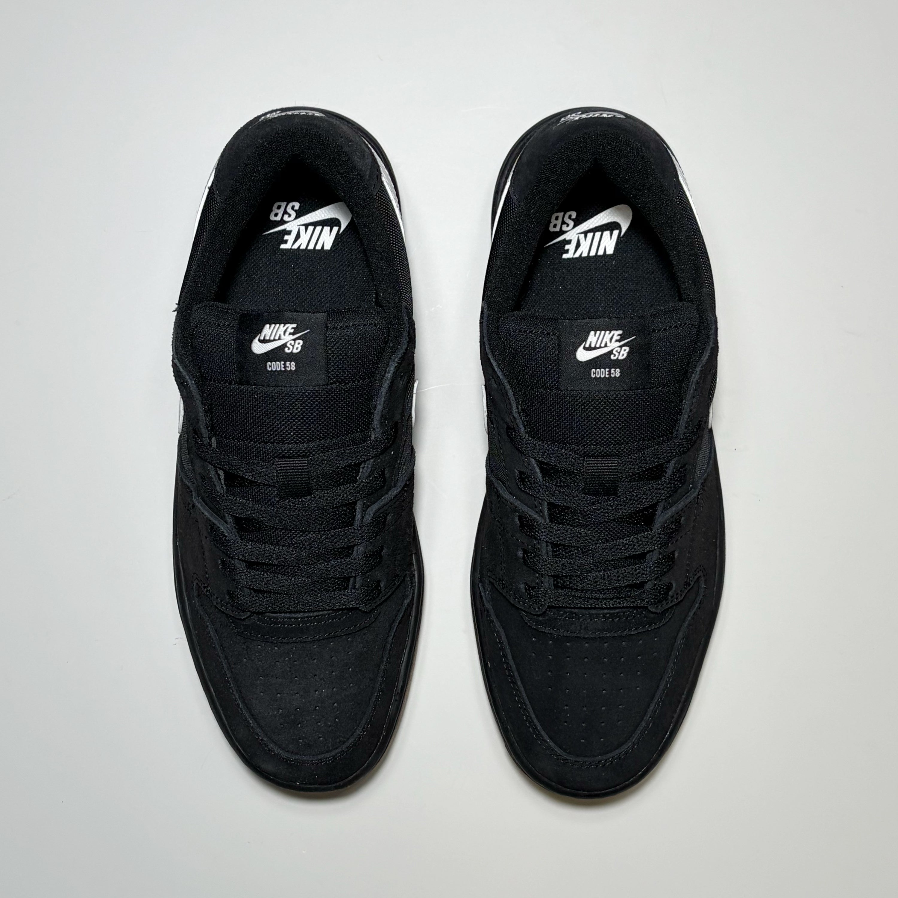 A pair of black Nike SB Code 58 sneakers with white logo details, shown from a top-down view on a light gray background.