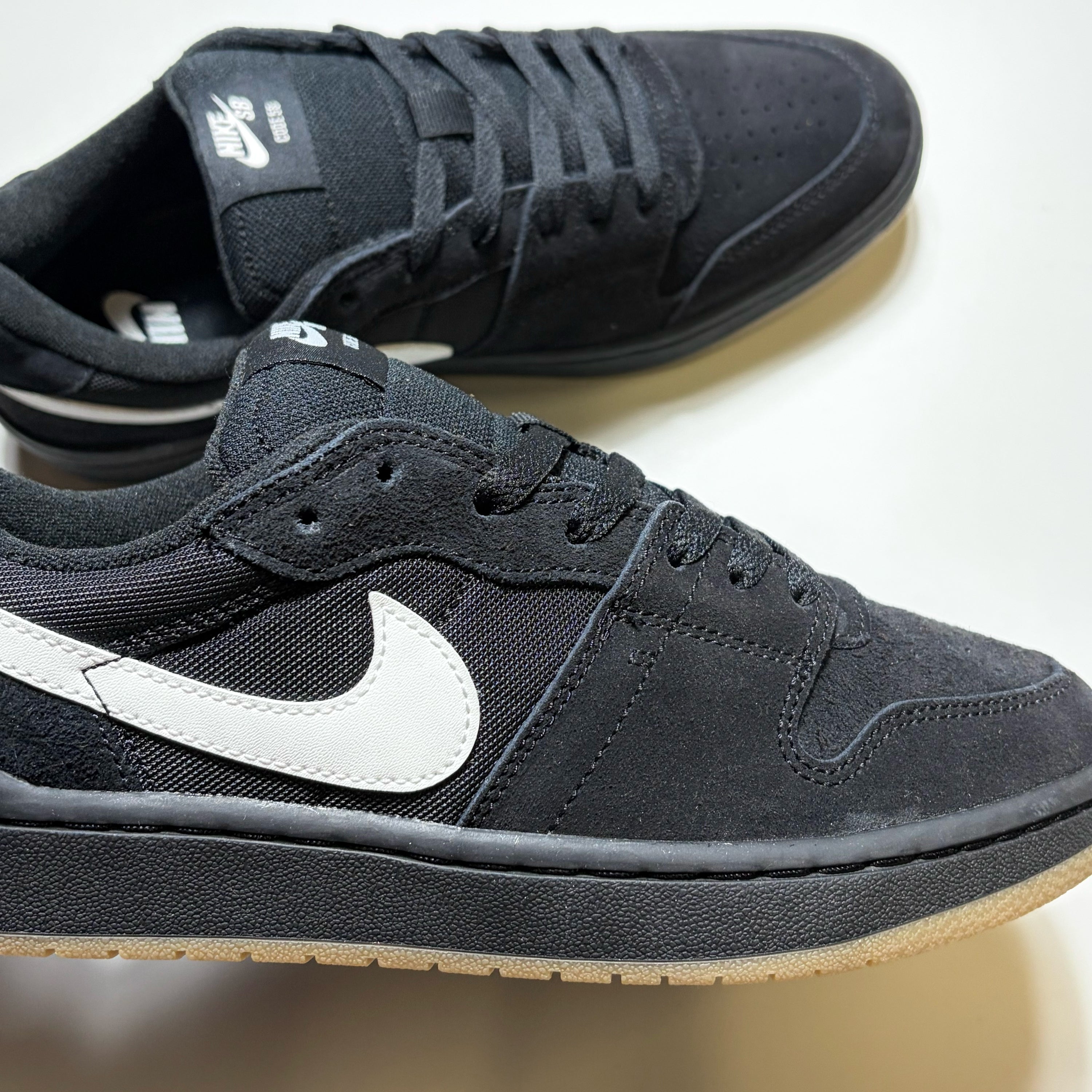 A pair of Nike SB Code 58 sneakers in black, featuring a black suede and mesh upper with a prominent white Swoosh on the side and a light beige gum sole.