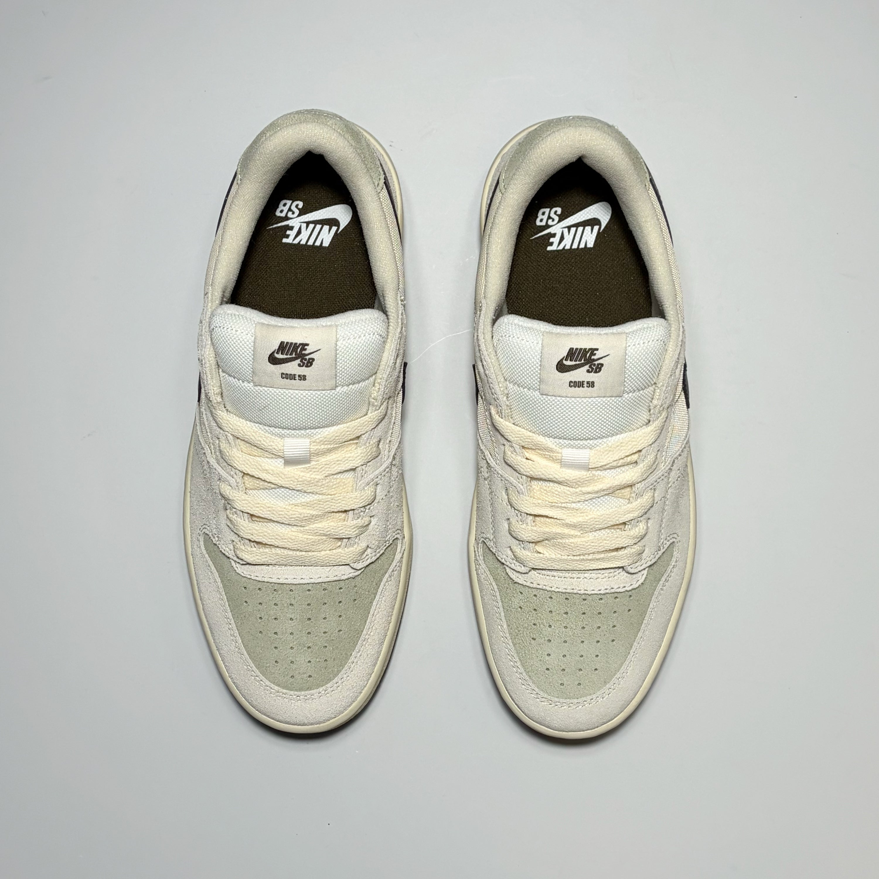 A pair of Nike SB Code 58 sneaker in off-white and light sage green, shown from a top-down view on a light gray background.