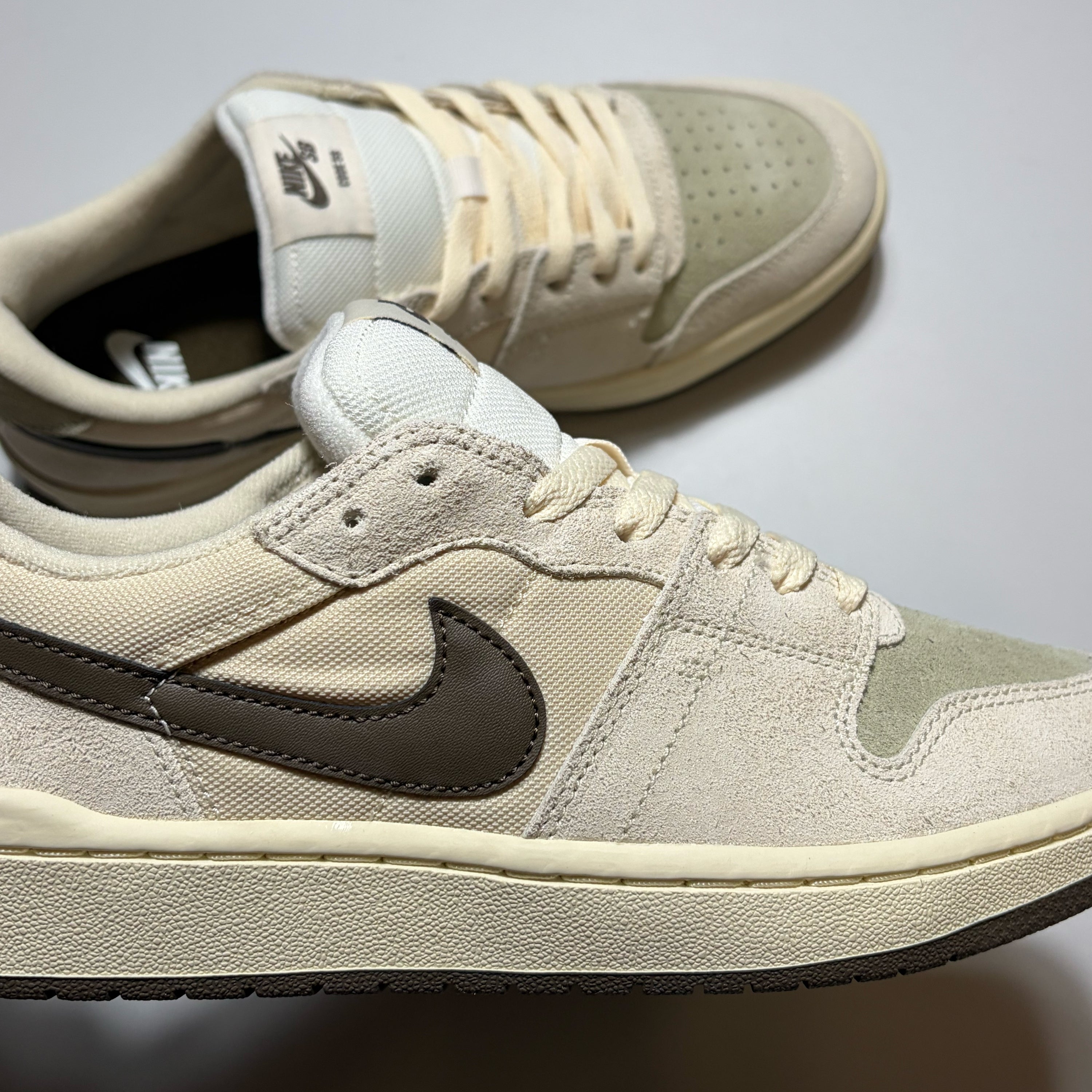 A pair of Nike SB Code 58 Low sneakers in a beige and off-white colorway, featuring a dark brown Swoosh and matching dark brown outsole.