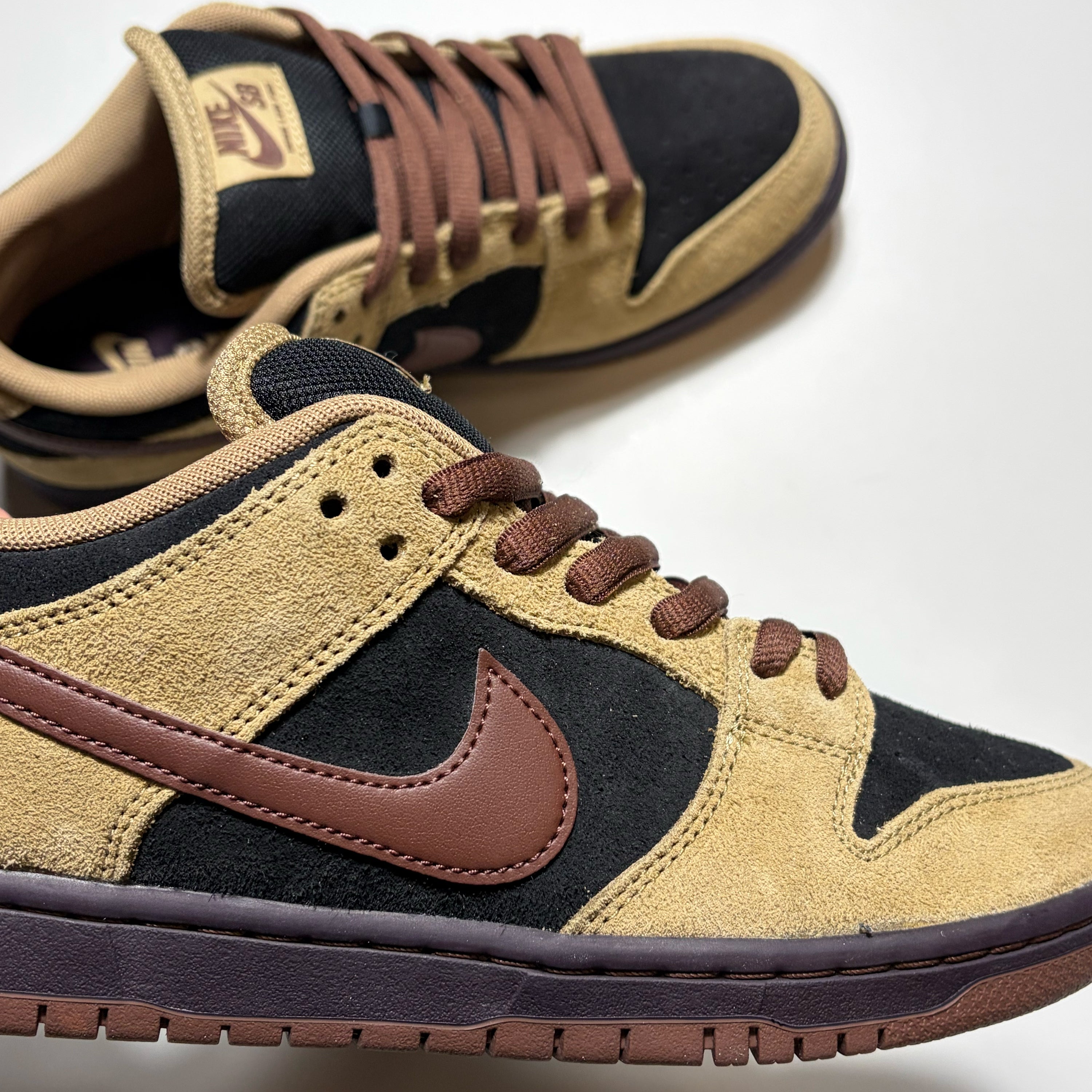 A pair of Nike SB Dunk Low sneakers in a brown and tan colorway, featuring suede and mesh panels, matching brown laces, and a brown Swoosh on a white background.