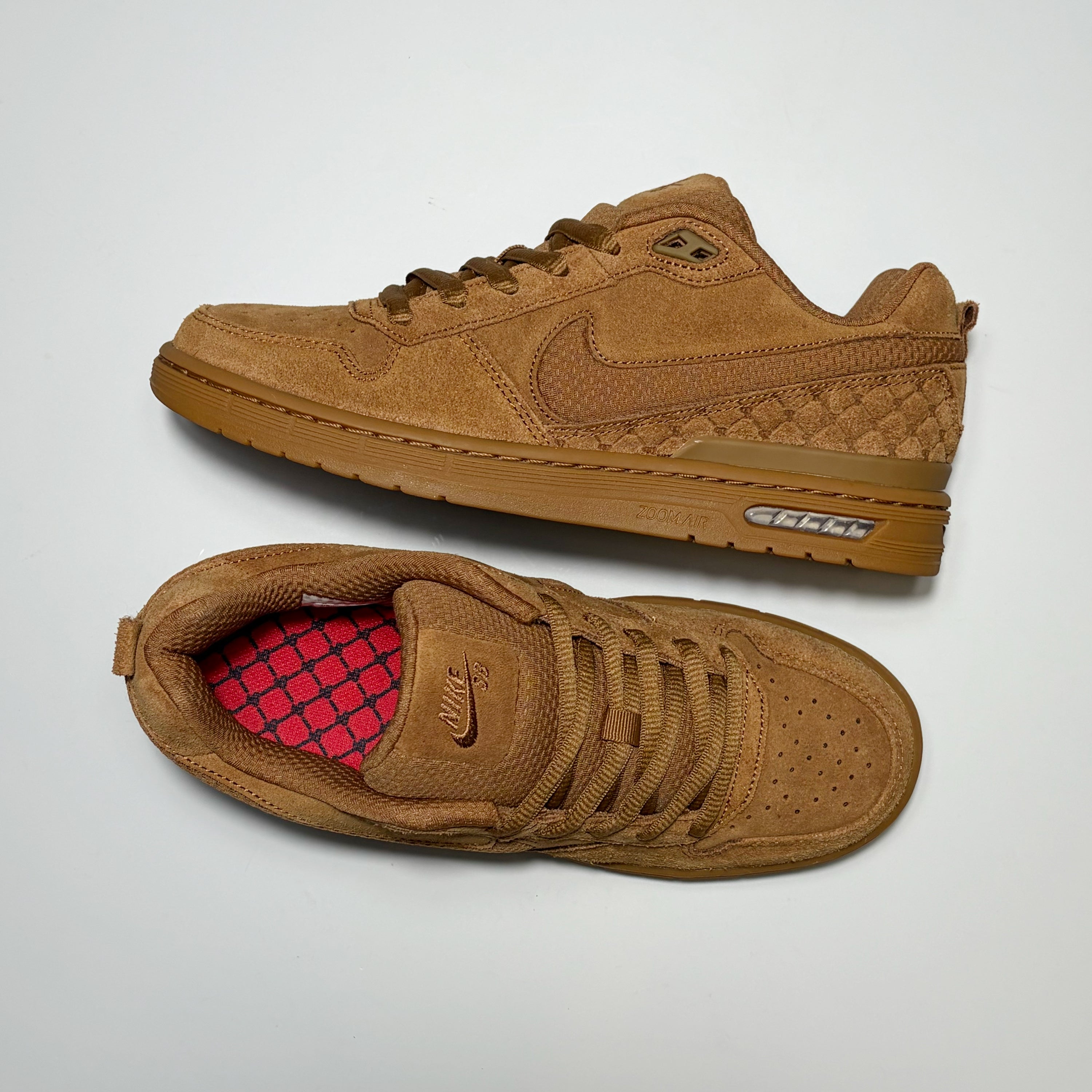 A pair of Nike SB Paul Rodriguez sneakers in a monochromatic tan/brown colorway, featuring suede and leather panels, a quilted heel, and a red patterned lining visible on the tongue of the bottom shoe.