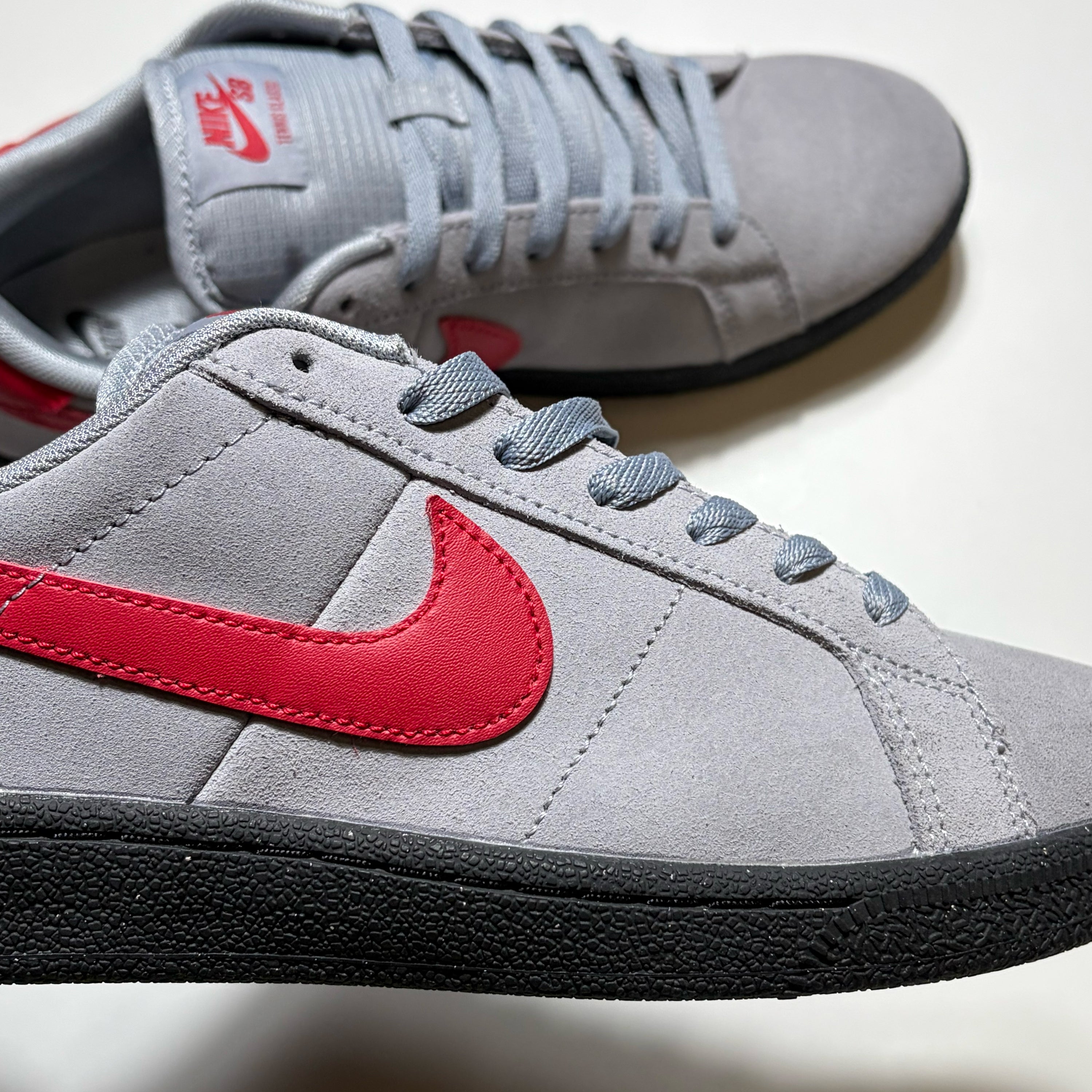 Close detail of Nike SB Tennis Classic stealth grey with red swoosh and black outsole.
