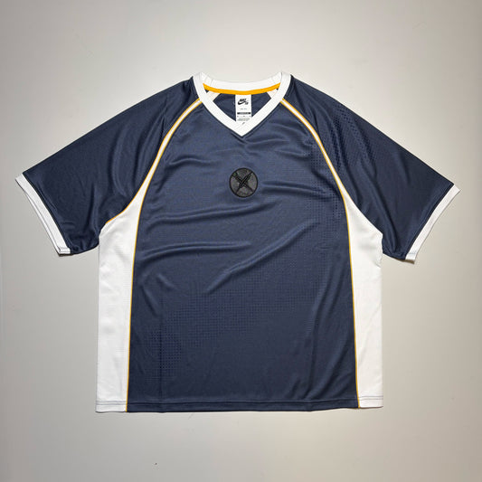 Nike SB Yuto Horigome short-sleeve athletic jersey laid flat on a light gray background. The jersey is navy blue with white side panels and collar trim, accented by thin yellow piping lines running down the center. 