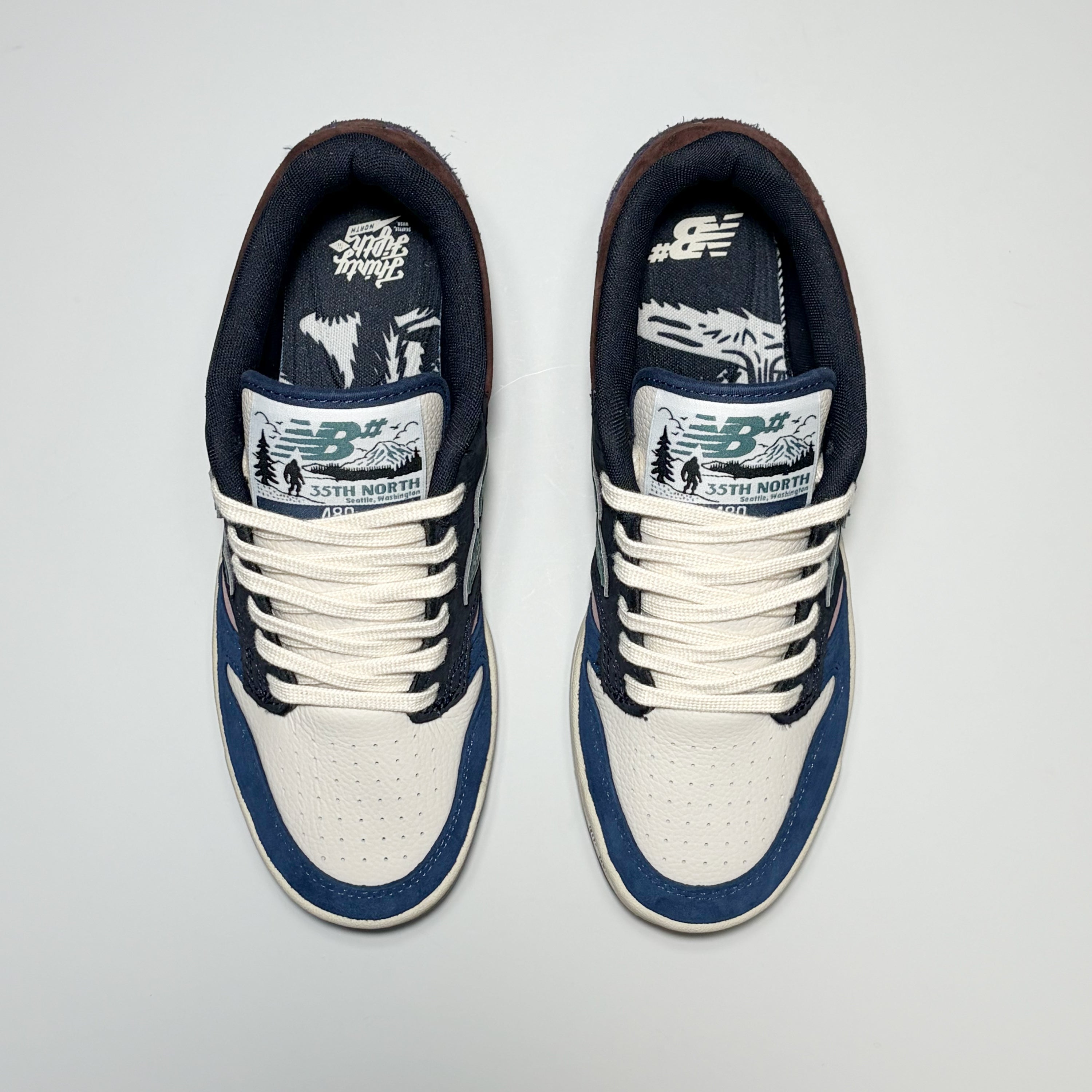 A pair of New Balance Numeric 480 sneakers in navy blue, white, and brown, shown from a top-down view on a light gray background.
