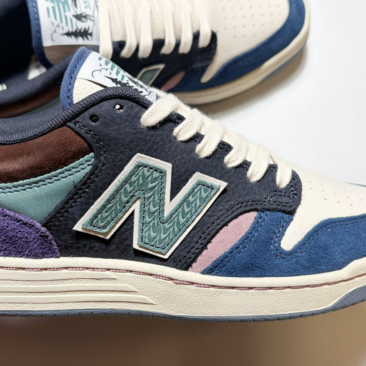 A close-up of a New Balance Numeric 480 featuring cream leather, navy suede, teal suede, brown leather, purple suede, and a pink accent panel, with a patterned green and white 'N' logo.