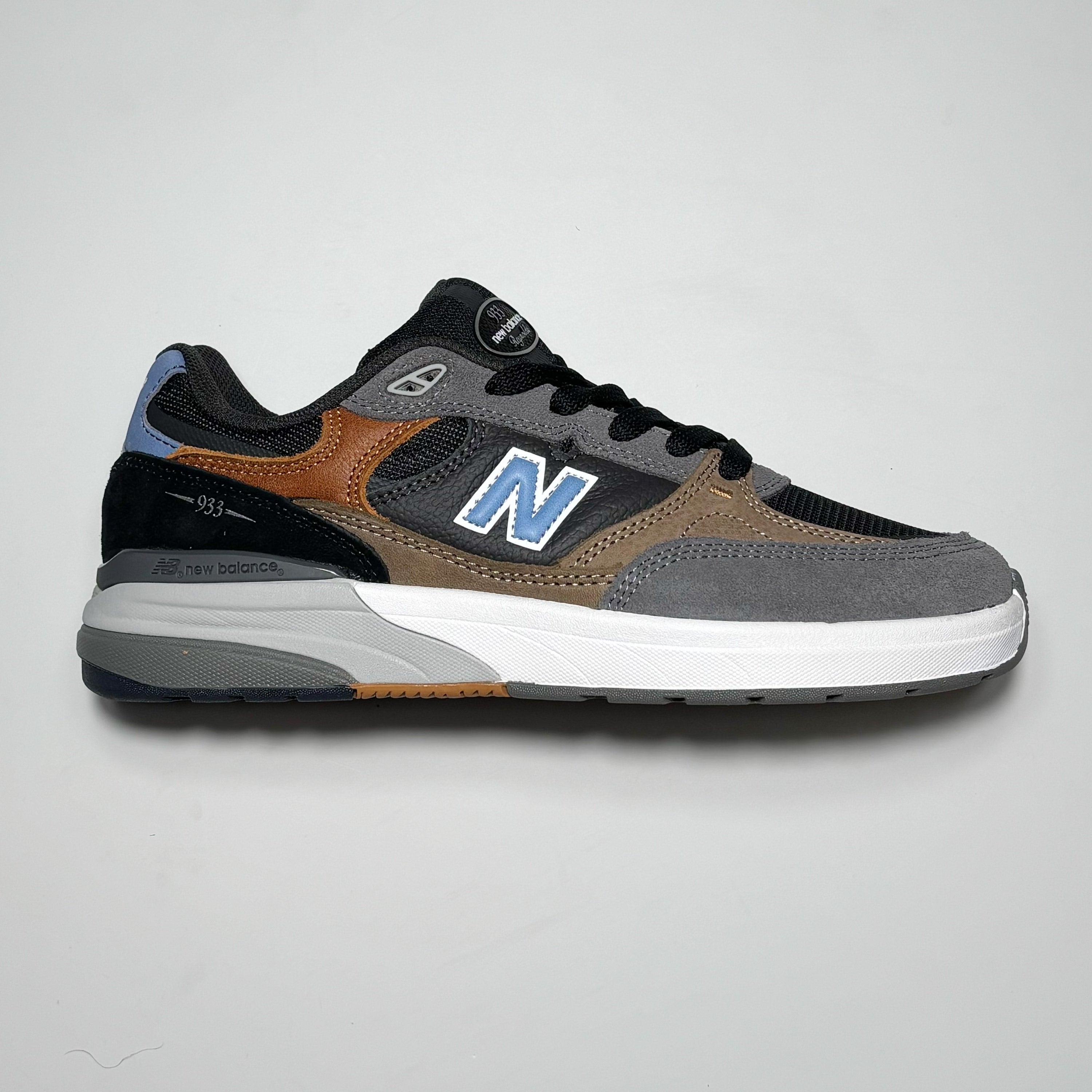 Side profile of right shoe. Grey, black, brown panels with blue N branding.