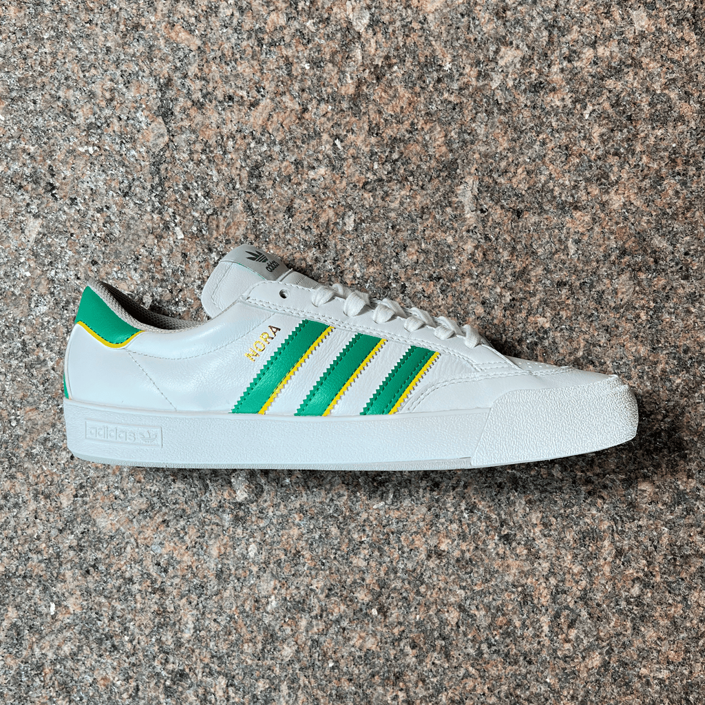 SIDE VIEW OF THE ADIDAS NORA PRO MODEL SHOE IN WHITE, GREEN AND YELLOW WITH WHITE SOLE DISPLAYED ON GRANITE