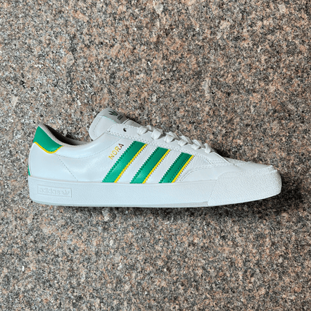 SIDE VIEW OF THE ADIDAS NORA PRO MODEL SHOE IN WHITE, GREEN AND YELLOW WITH WHITE SOLE DISPLAYED ON GRANITE